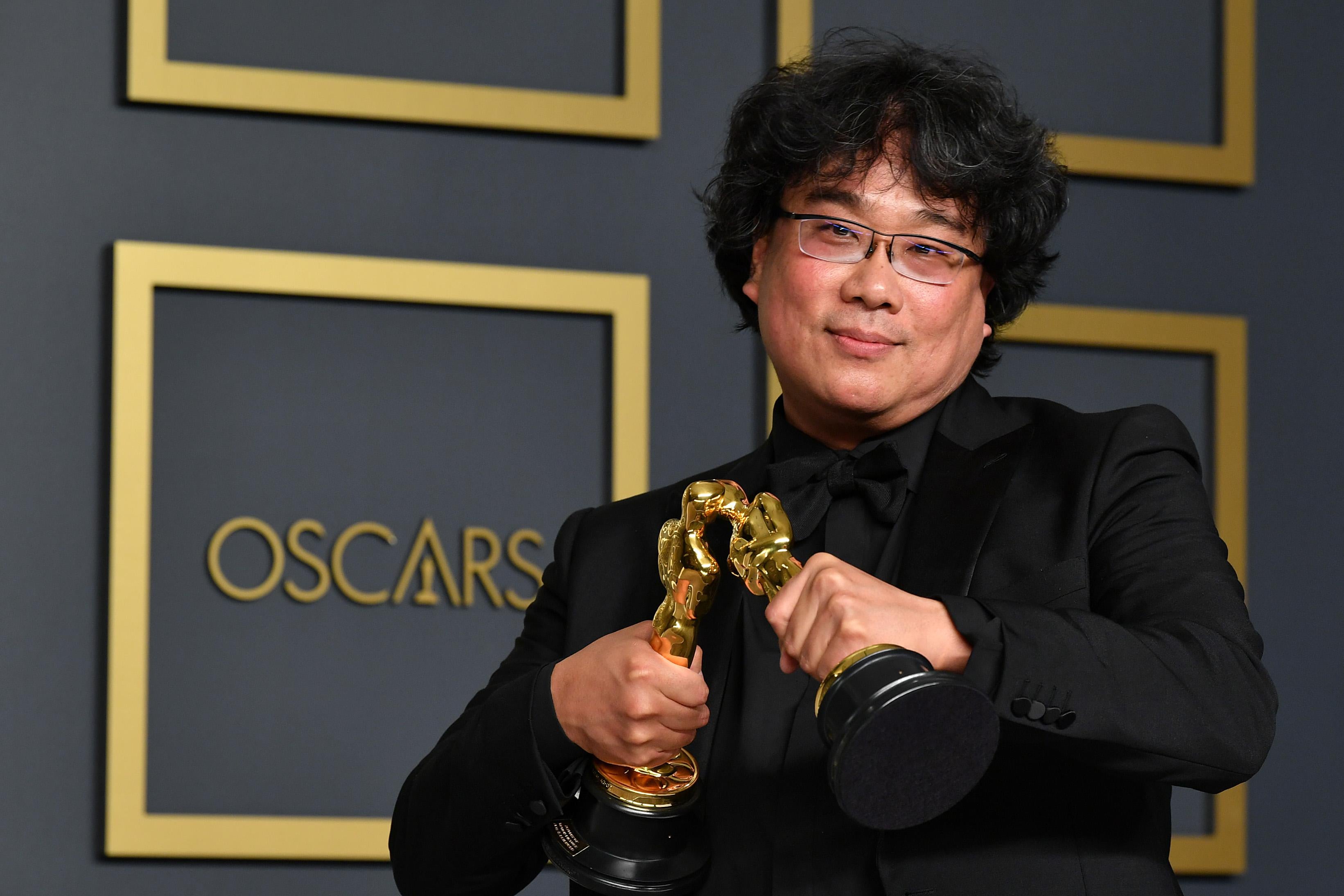 Bong Joon-ho smooshes the faces of two of his Oscars together so they kiss.