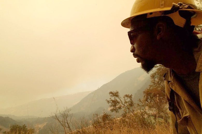 Brandon Smith, in firefighter gear, looks up at the sky, which is hazy with wildfire smoke