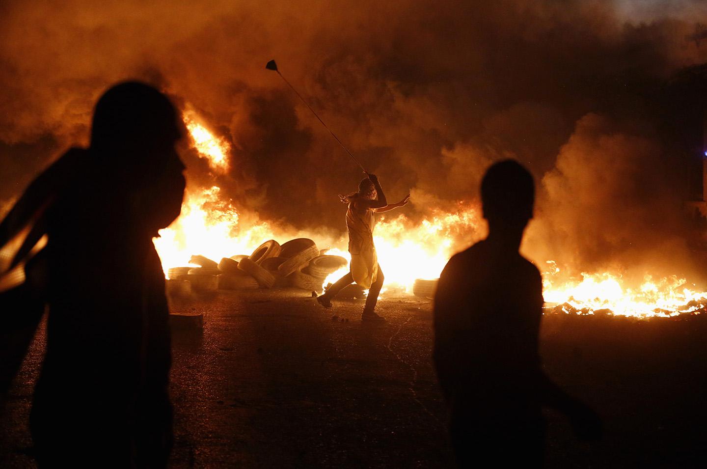 A Palestinian protester uses a slingshot to hurl stones toward Israeli troops during clashes, at a protest against Israeli offensive in Gaza.