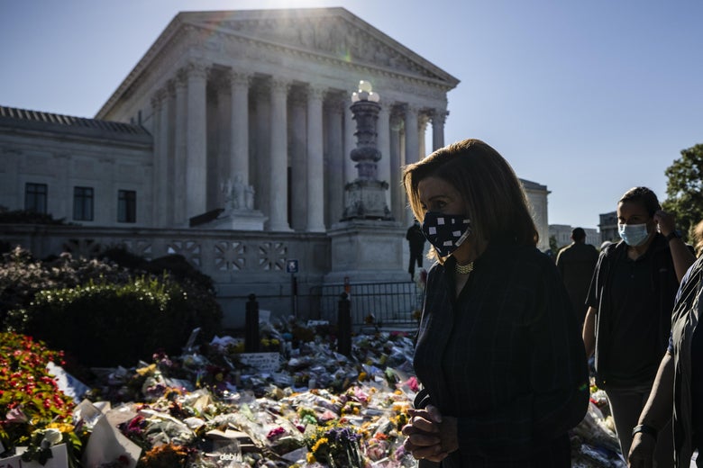 Pelosi, wearing a stars and stripes mask, walks past a memorial of flowers for RBG.