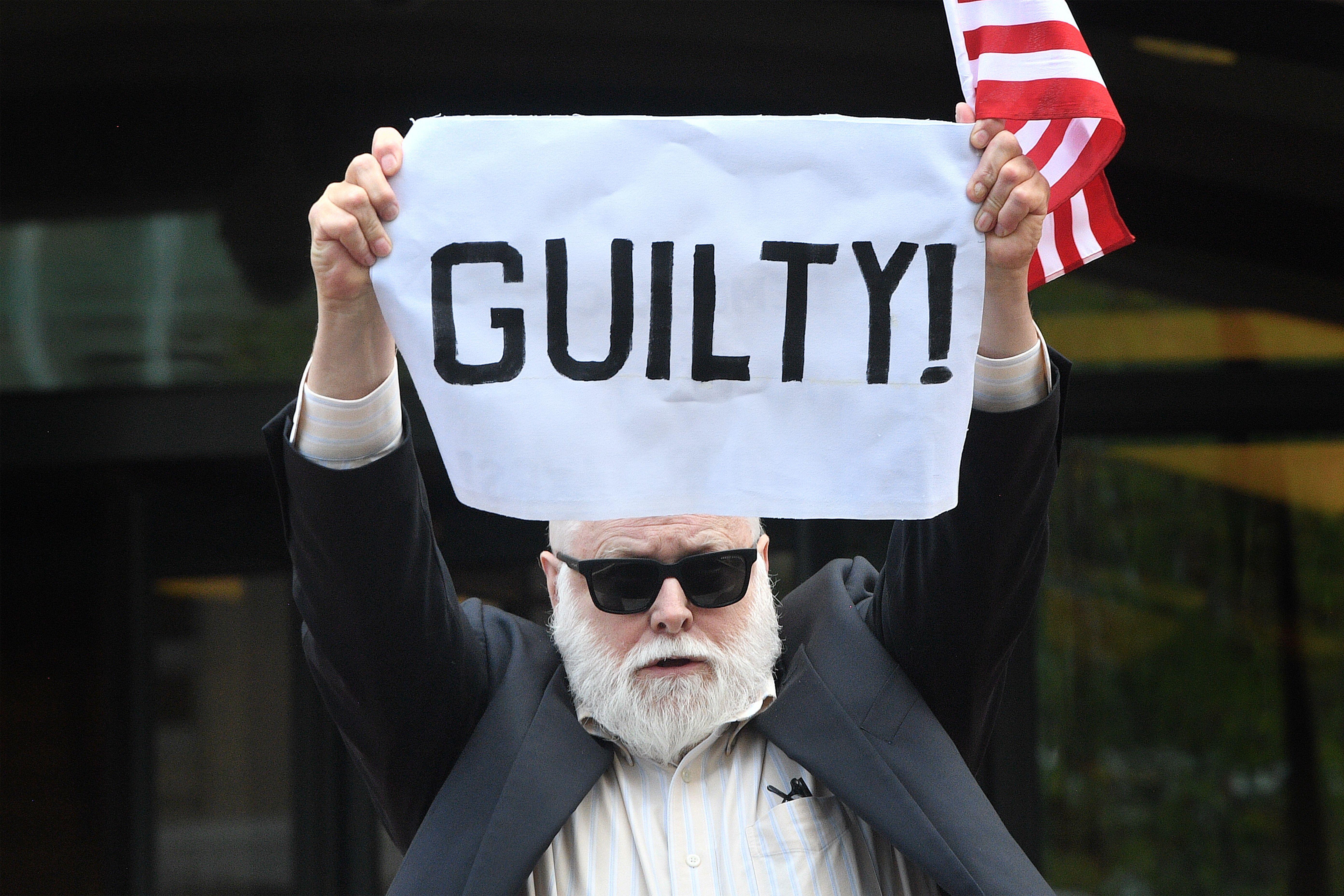 A bearded man with sunglasses holding a large white cloth reading "Guilty"