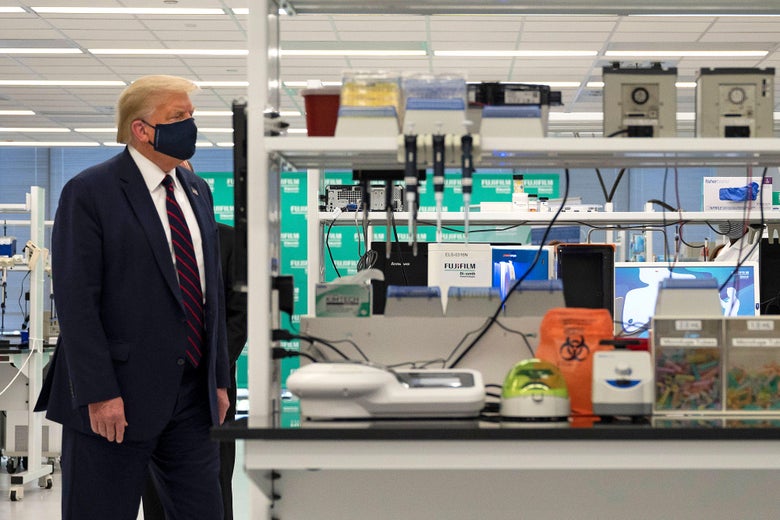 Trump wears a suit and a mask as he walks by scientific equipment.