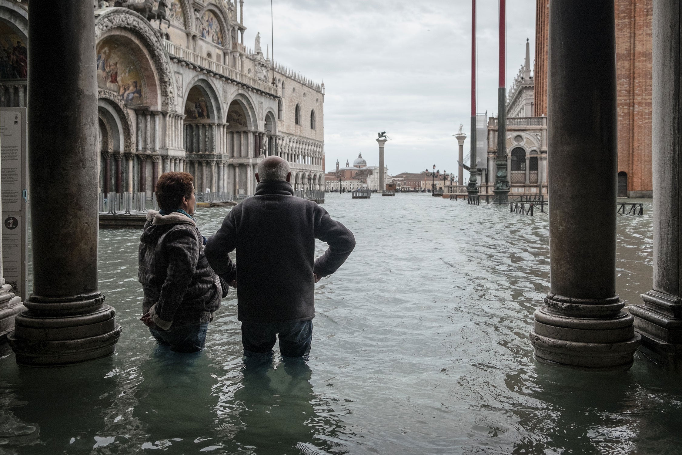 Two people observe a flooded St. Mark's Square, with water reaching their thighs, Nov 15th 2019, Venice.