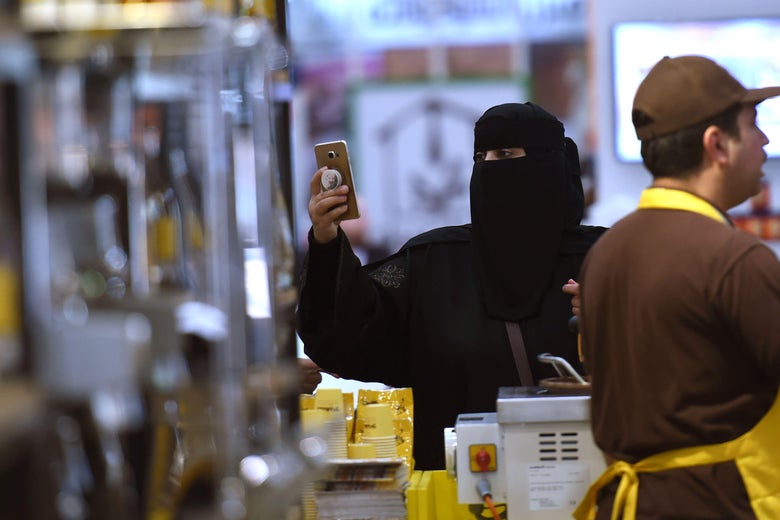 A Saudi woman holds up her cellphone next to a stand at the International Coffee and Chocolate Exhibition. 