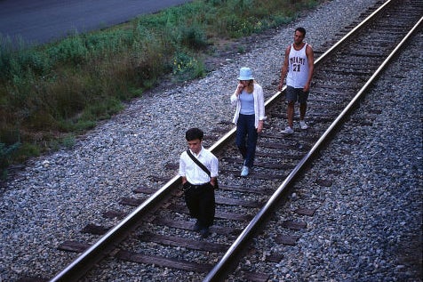 A movie still featuring three people on a train track.