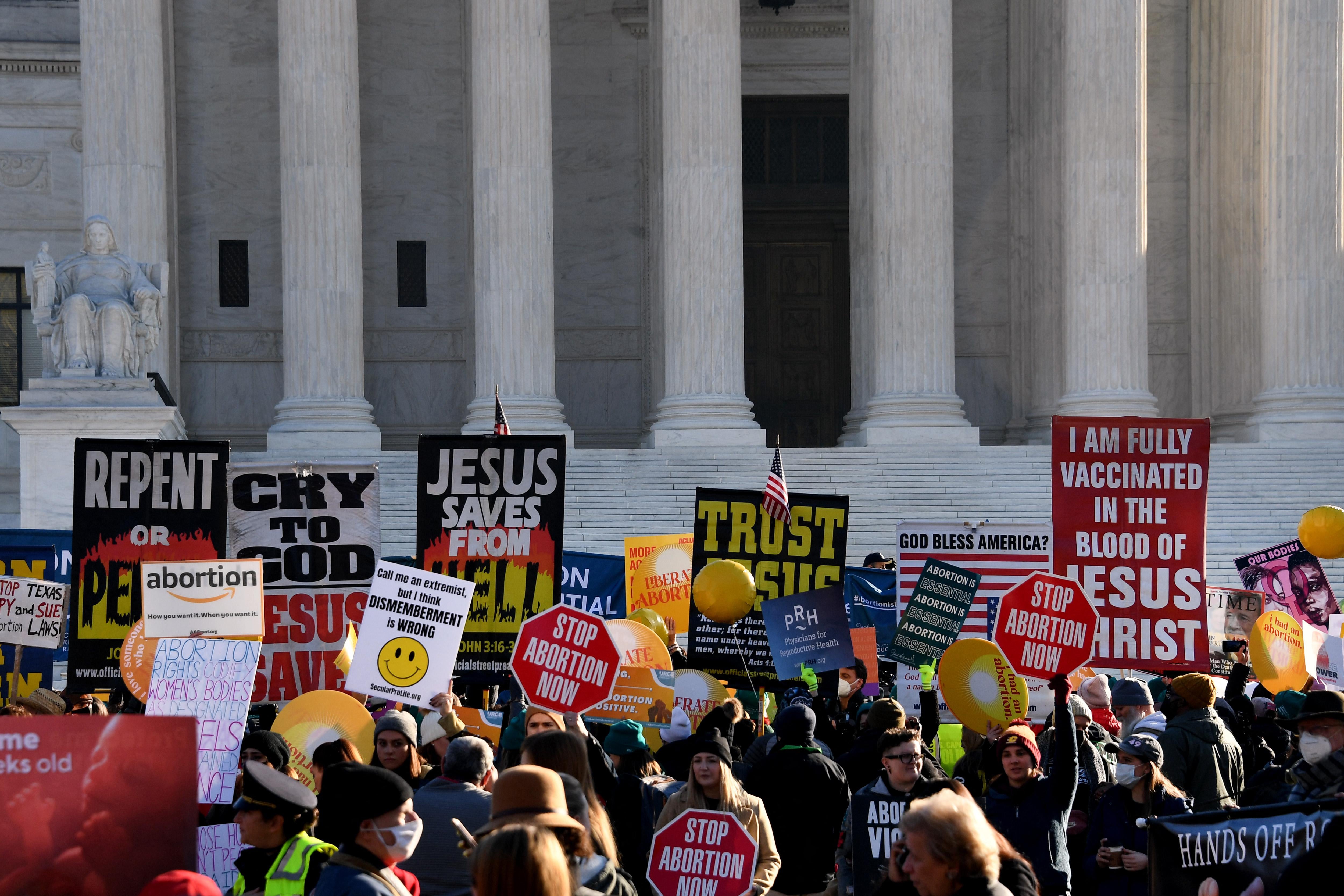 A crowd of people in front of the court steps holding signs with slogans such as "I am fully vaccinated in the blood of Jesus Christ," "Stop abortion now," and "Trust Jesus"
