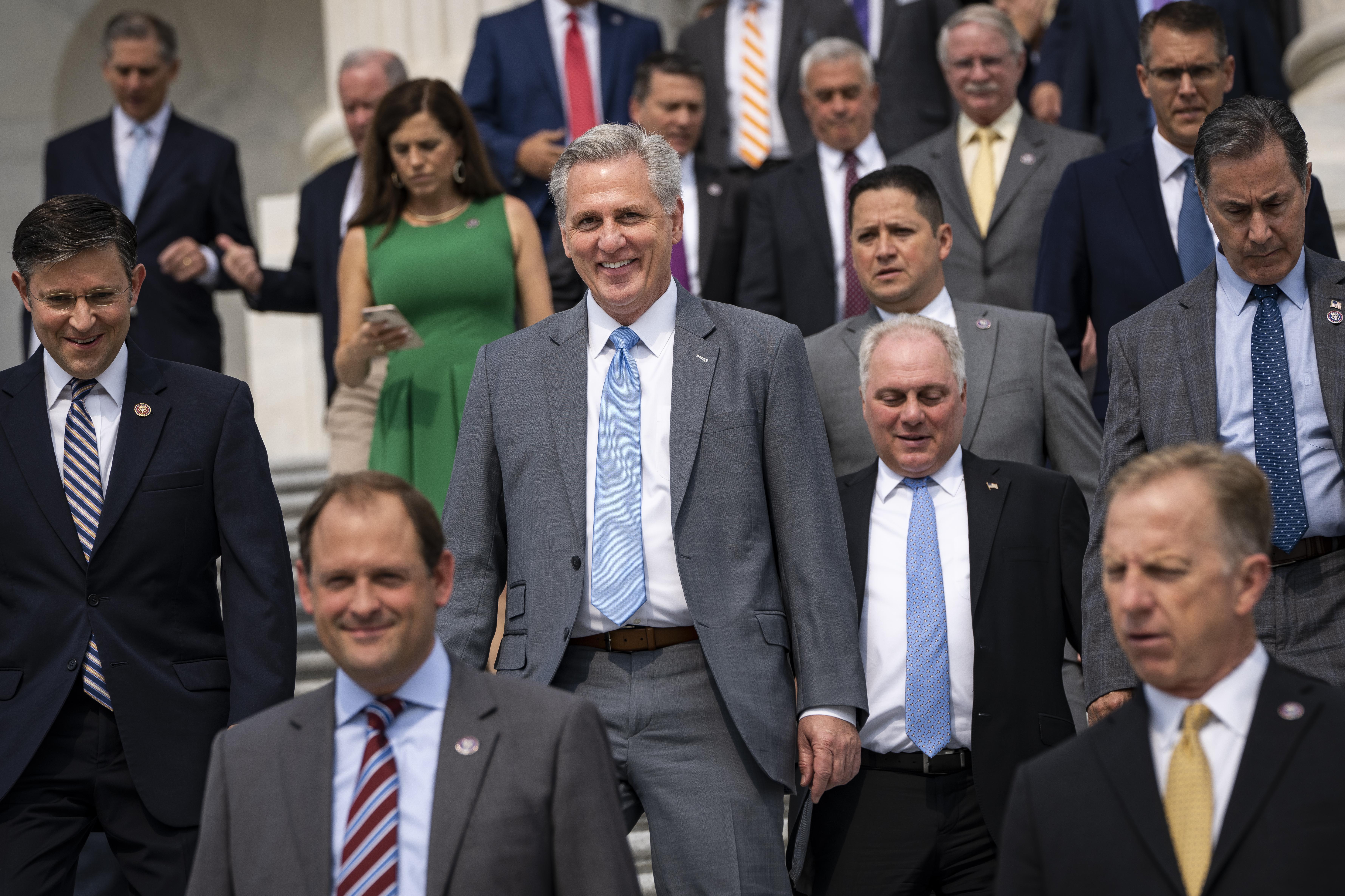 A bunch of old white men in suits walking down stairs, along with one white woman