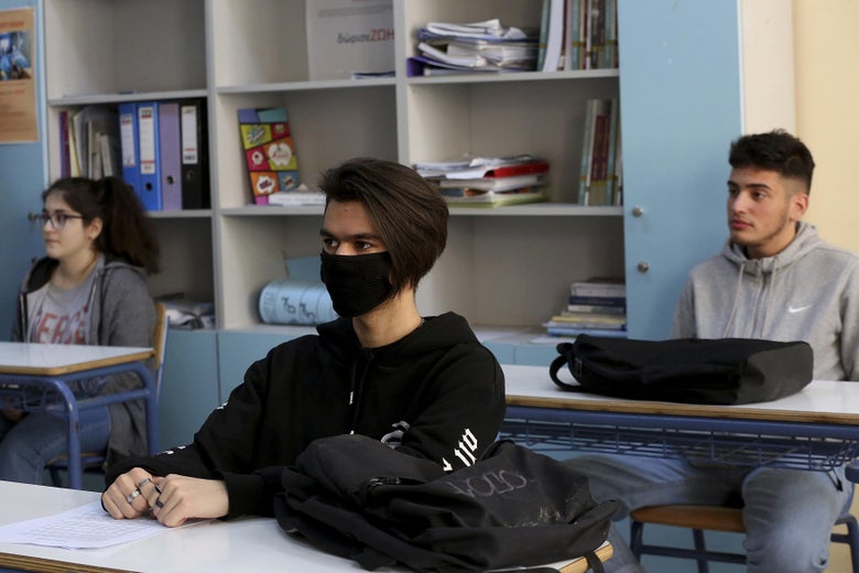 Three students, one wearing a mask, sitting at desks in a classroom