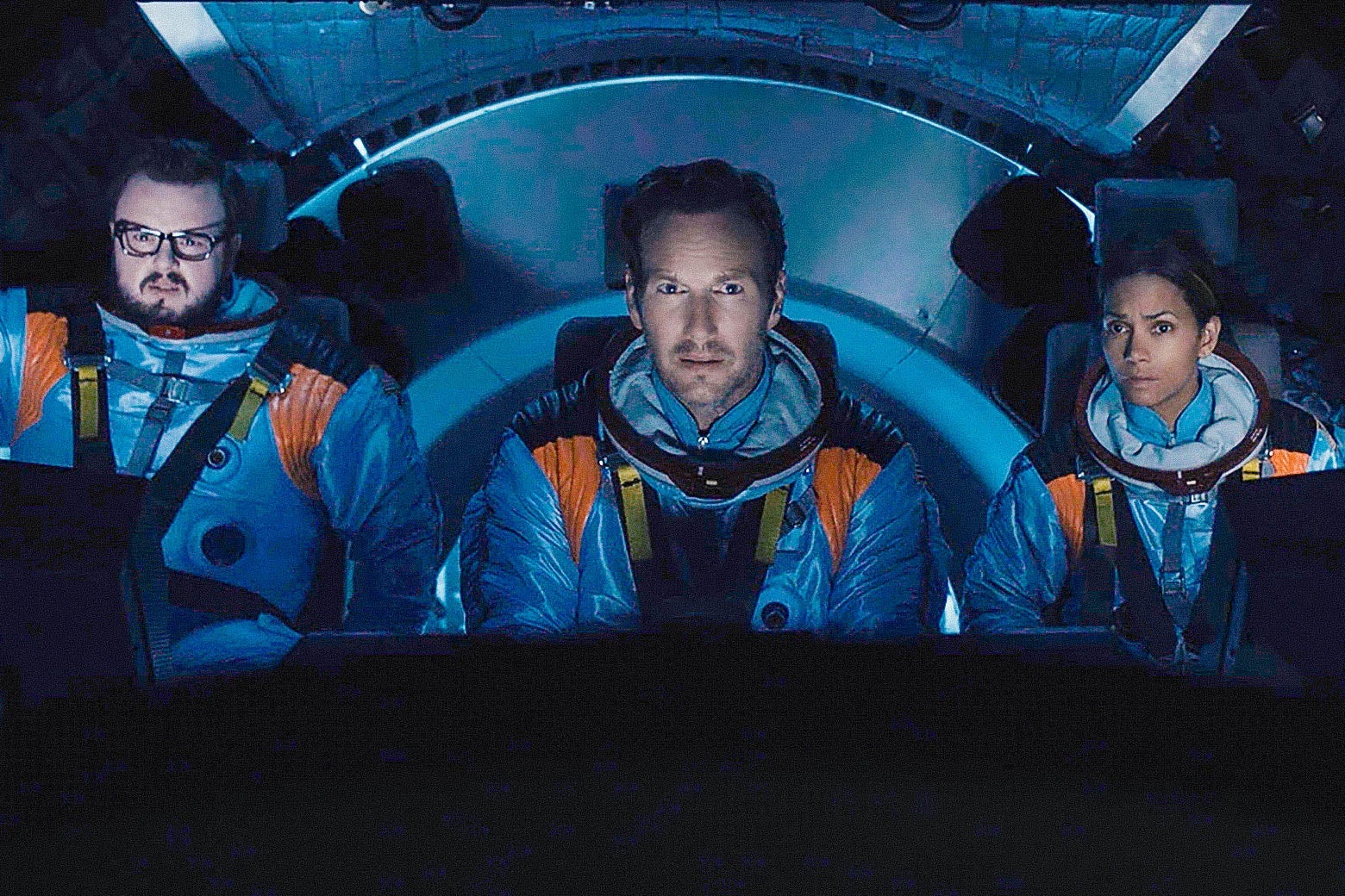The three actors in spacesuits in a cockpit. 