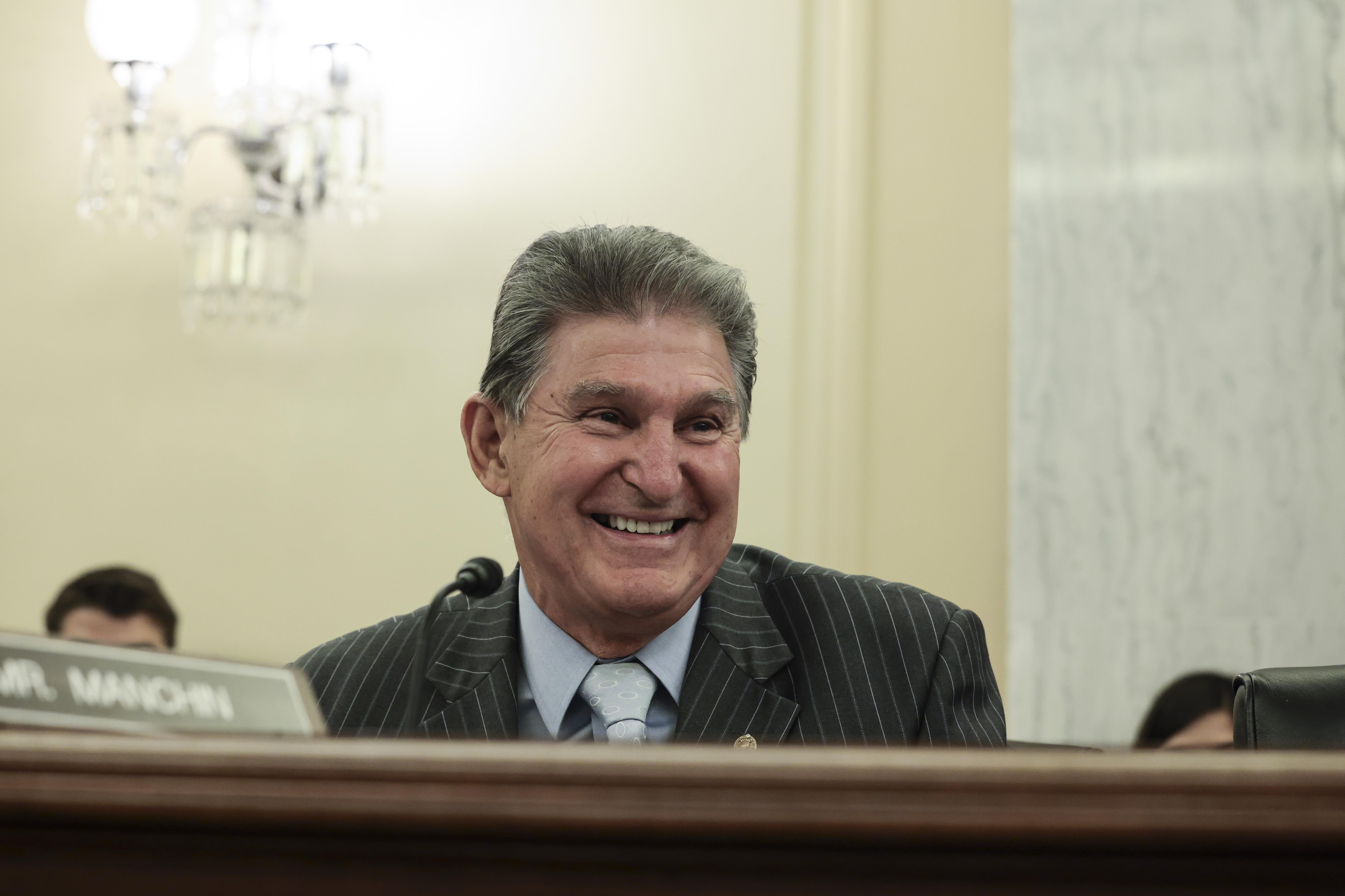 Joe Manchin sits smiling at a table with a nameplate reading "Mr. Manchin."