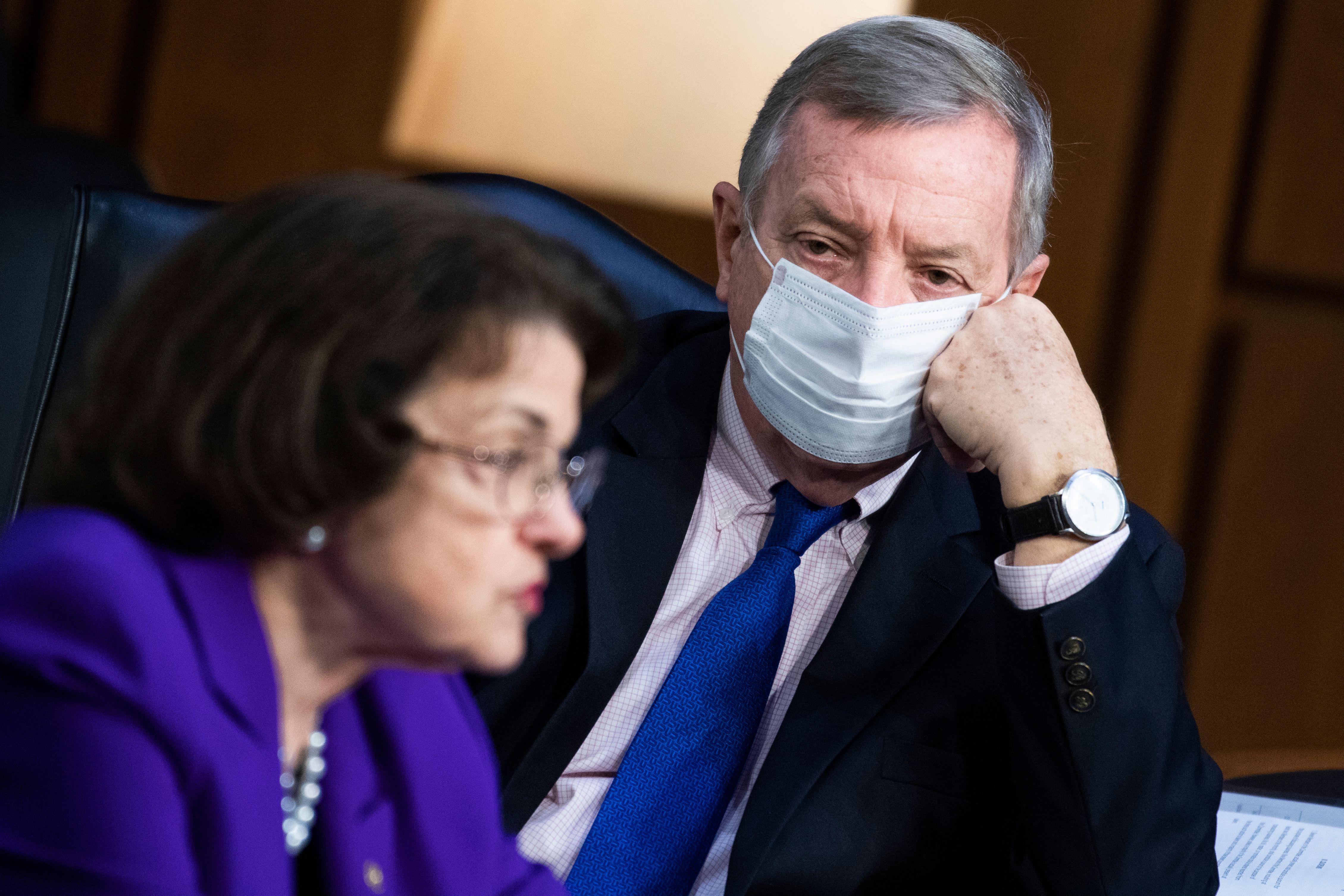 Durbin, wearing a mask, stares at Feinstein, who's face is blurred.