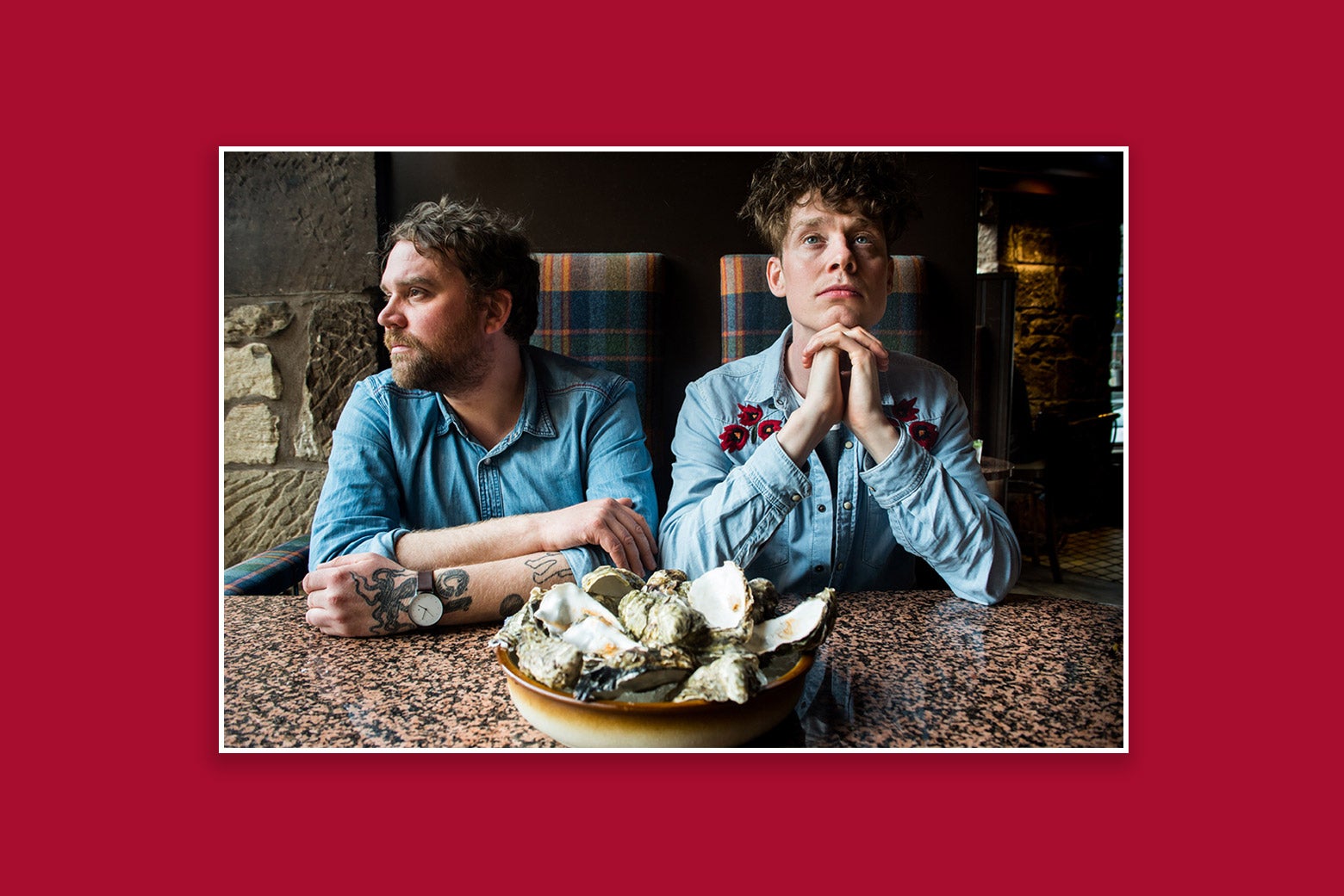 Two men sit in front of a table, a plate of oysters before them.