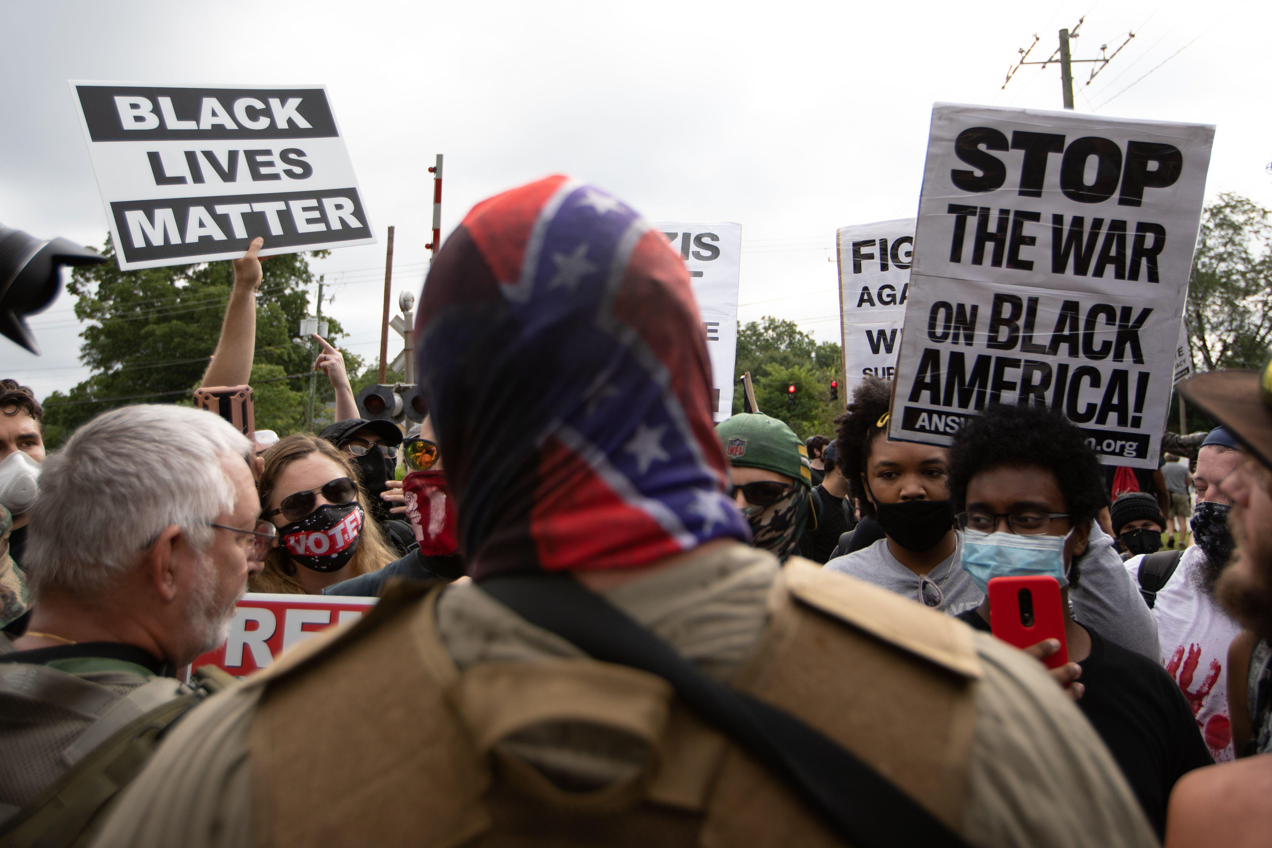 A man in a Confederate flag bandana faces BLM and other anti-racist protesters