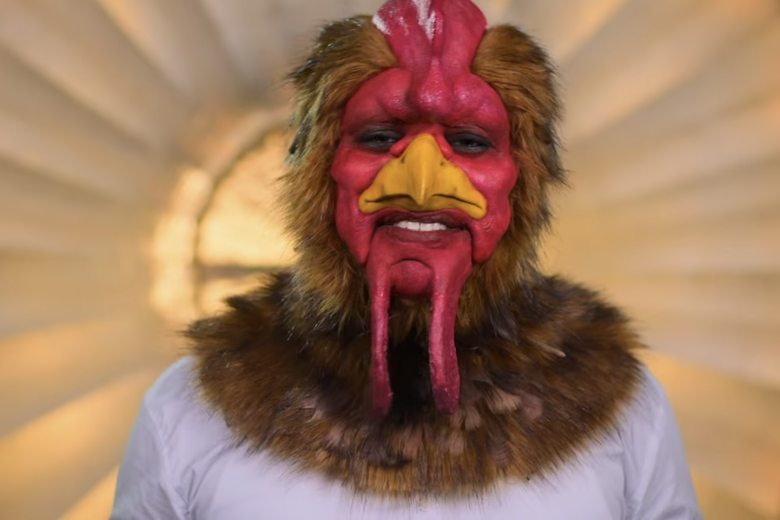 Man in white shirt smiling at the camera while wearing a rooster head.