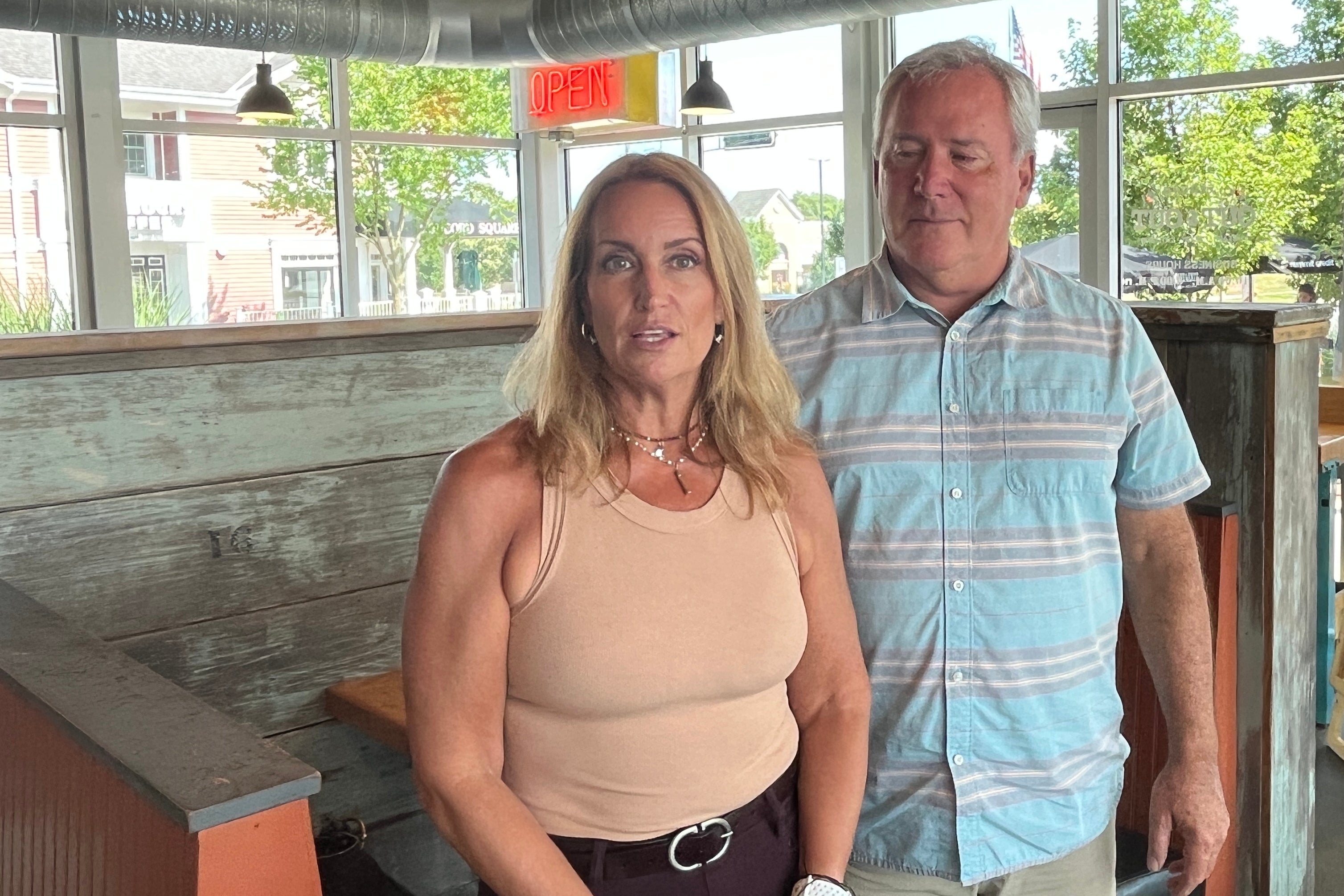 A white woman with blond hair stands next to a gray-haired man in a polo shirt.