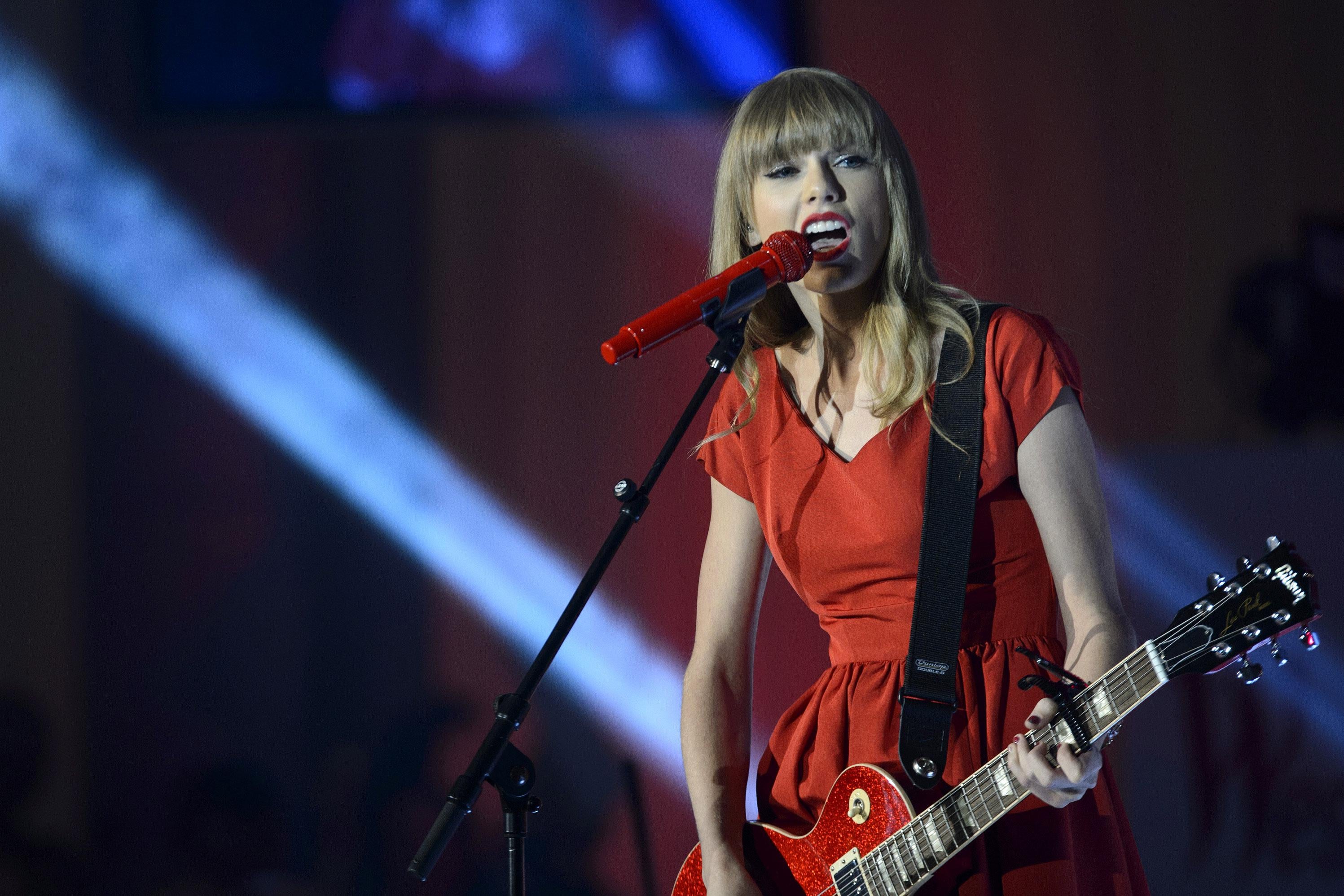 A blond plays a red guitar while wearing a red dress on stage. 