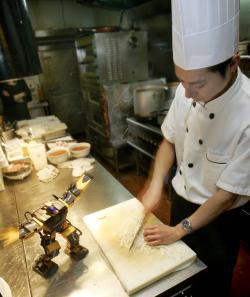 A robot performs pre-programed actions as a chef (R) prepares food in the Robot Kitchen restaurant.