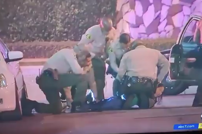 Four uniformed officers surround the reporter lying face-down on the pavement