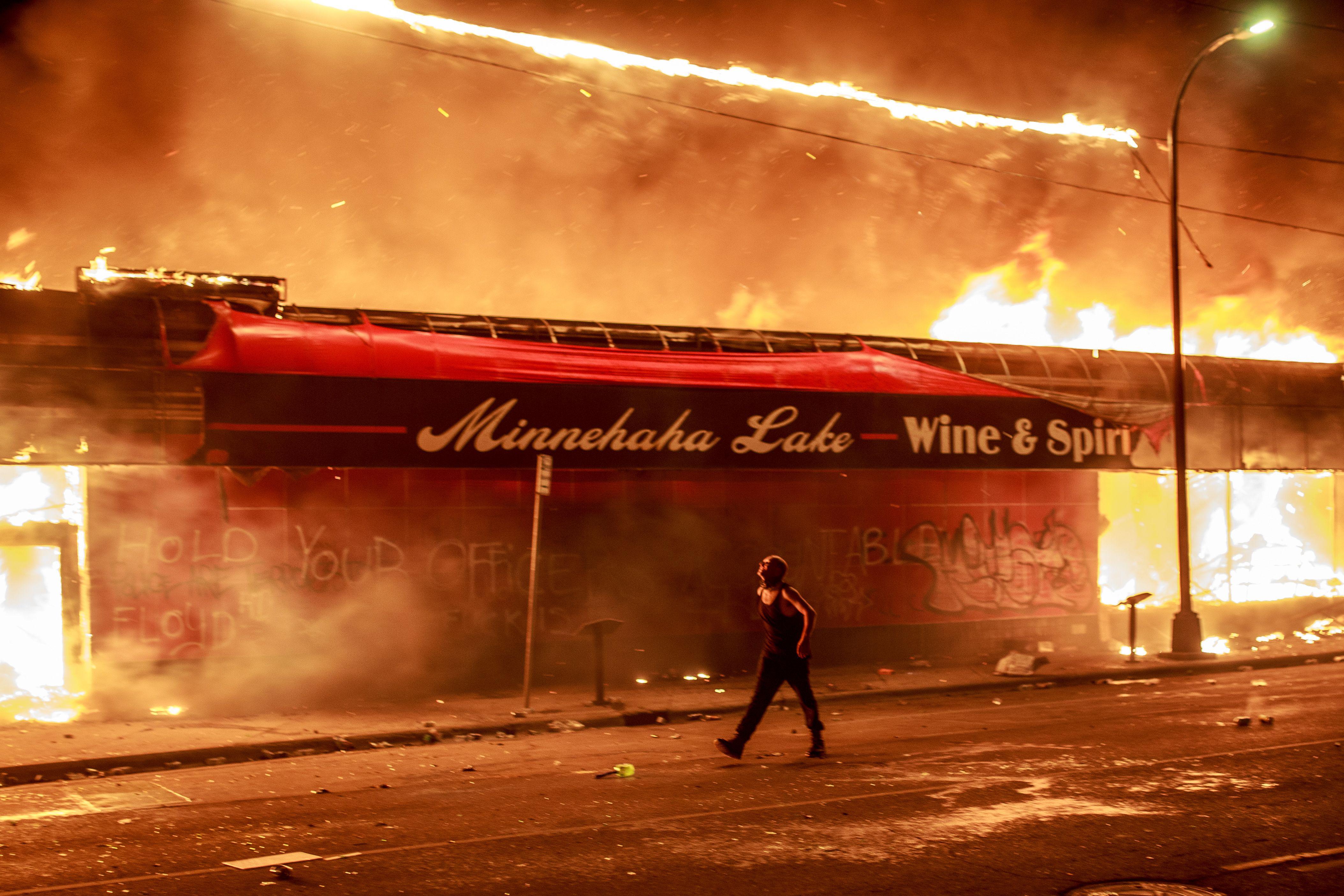 A man walks past a burning building
