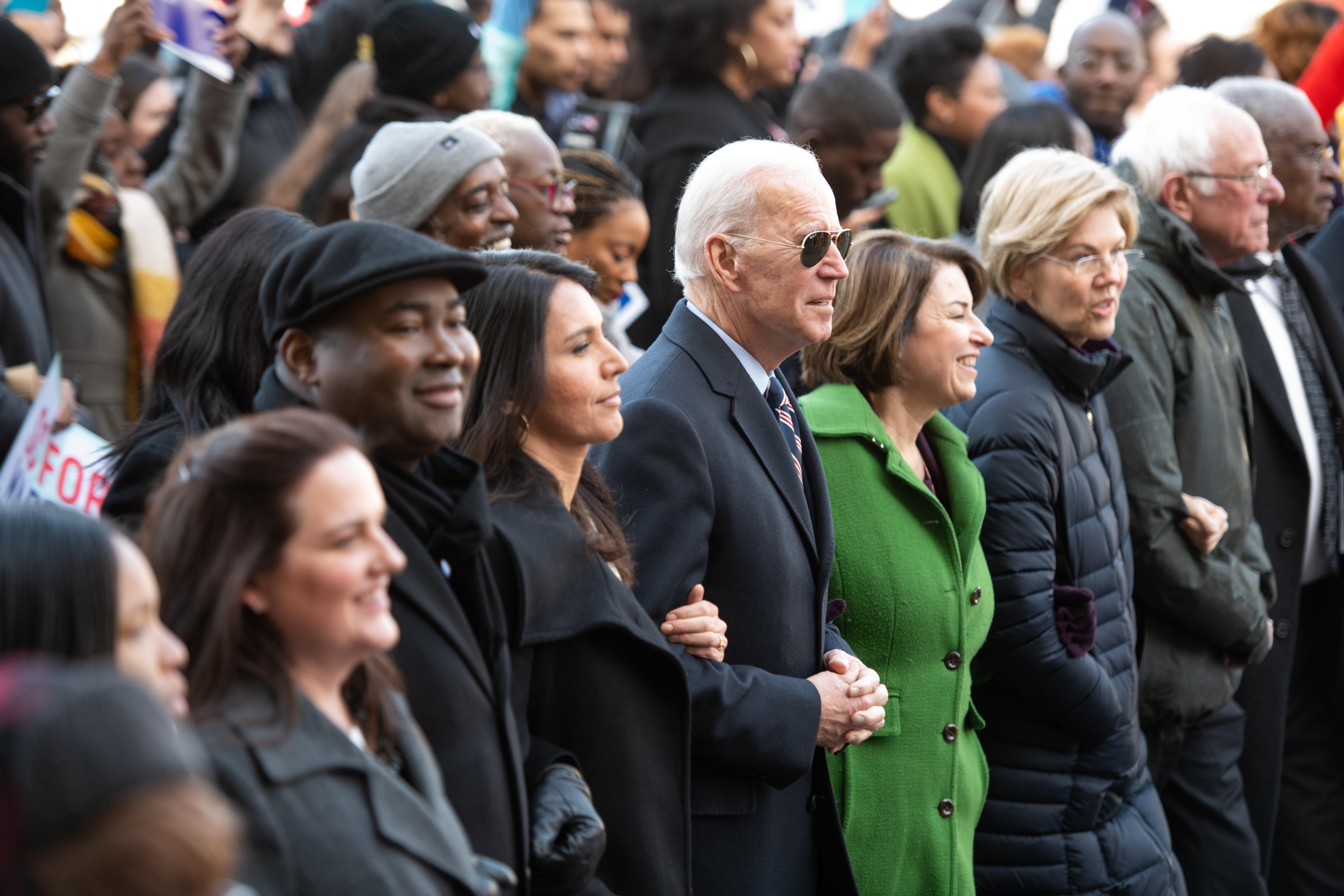 Tulsi Gabbard, Joe Biden, Amy Klobuchar, Elizabeth Warren, and Bernie Sanders link arms in a row of marchers.