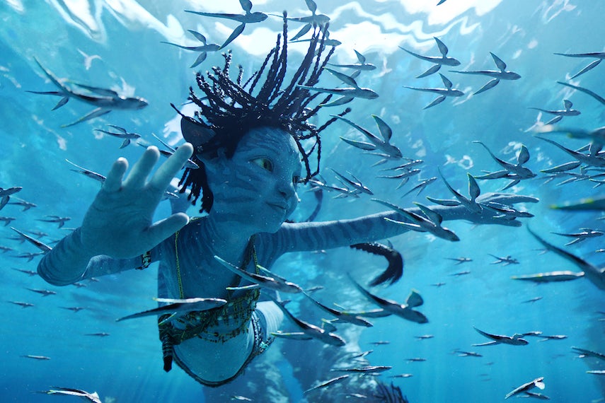 A humanlike blue creature swims through a school of fish.