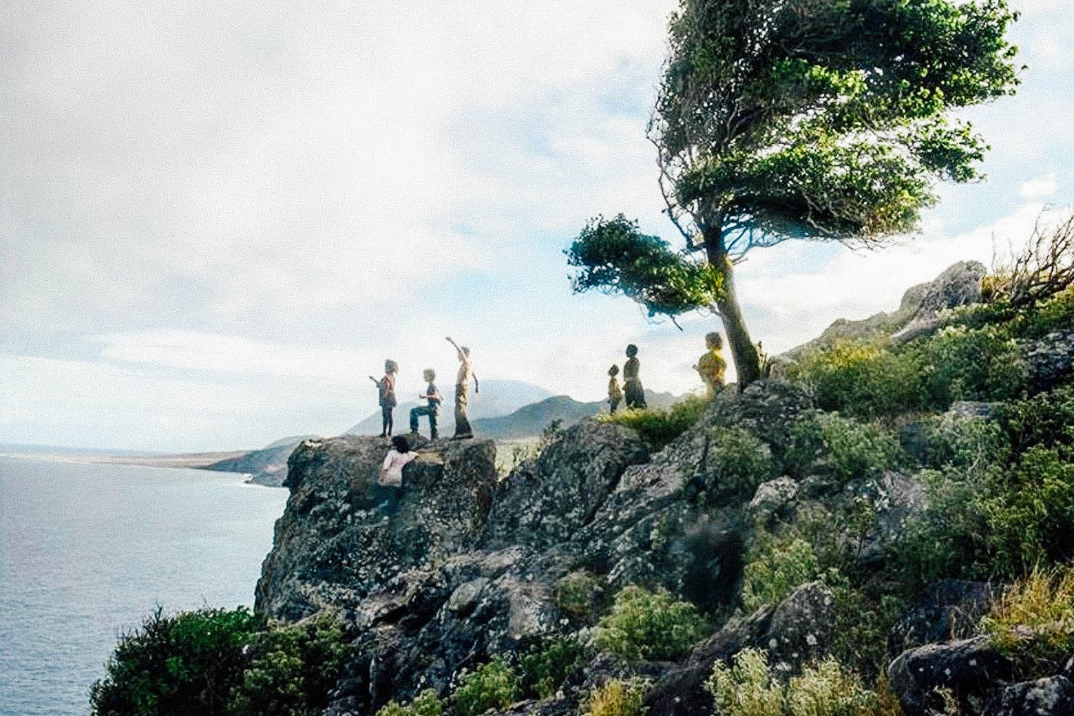 A scene from Wendy, in which a group of kids stand on a foliage-heavy cliff overlooking a body of water