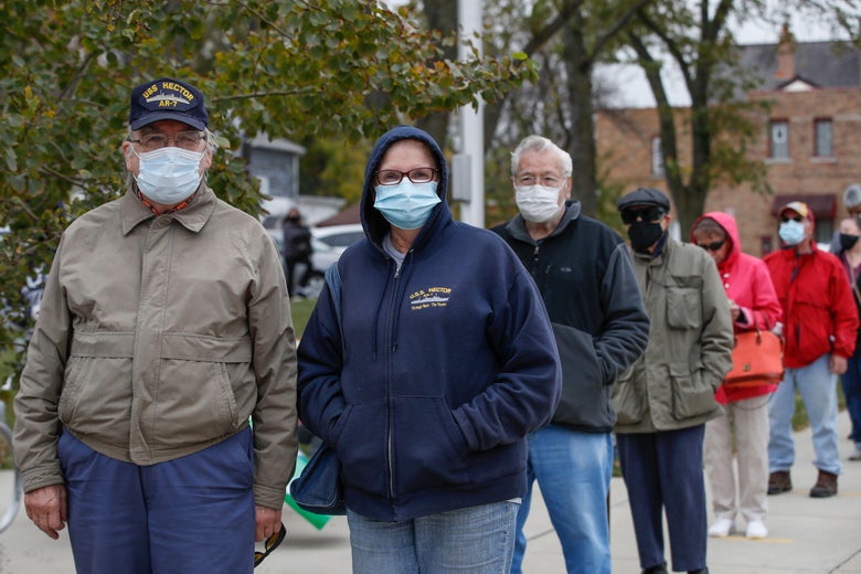 A line of people outside wearing masks waiting to vote