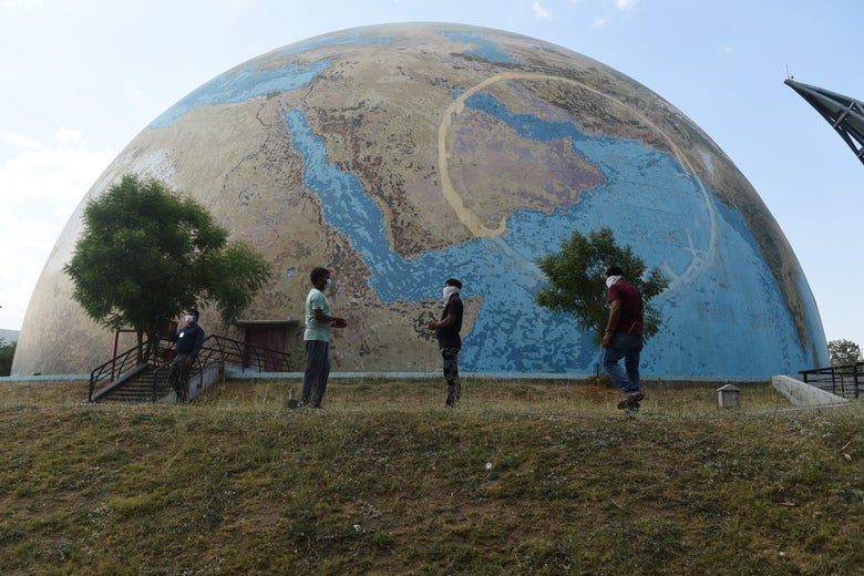 People in masks stand in front of a model of Earth.