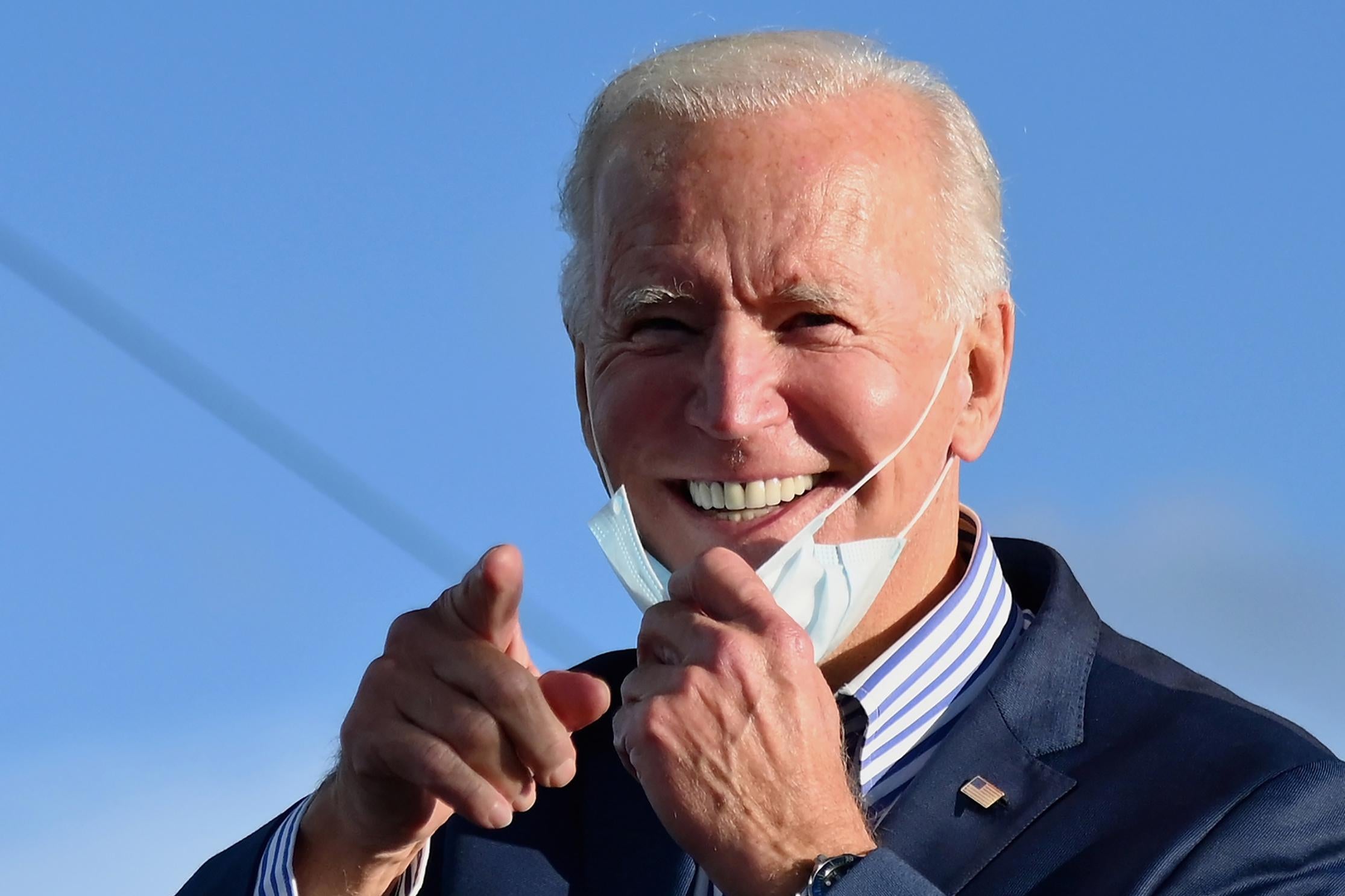 Biden grins, pulling his mask down with one hand as he points toward the camera with the other hand