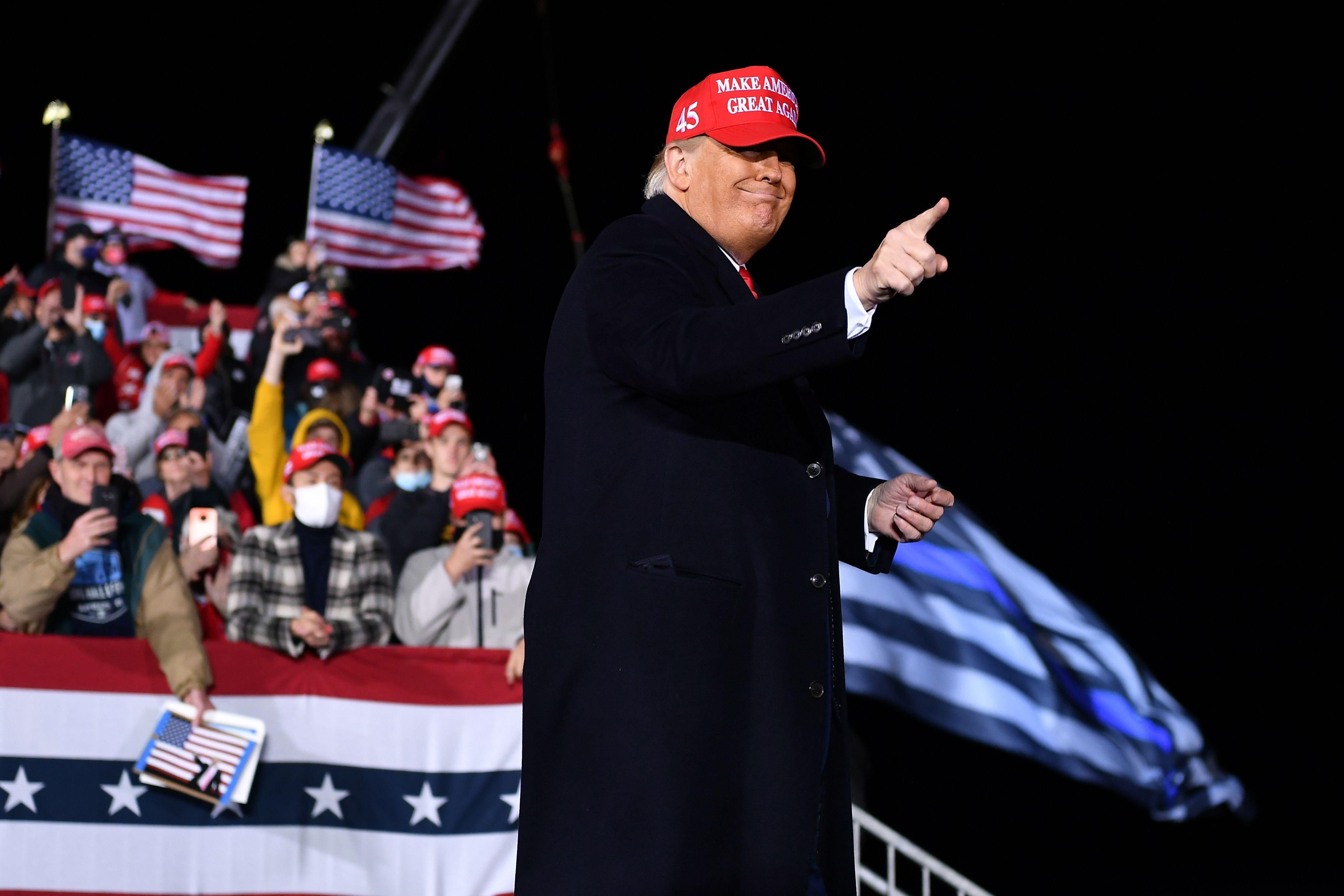 Trump, wearing a MAGA hat, points and smiles before a crowd of his supporters