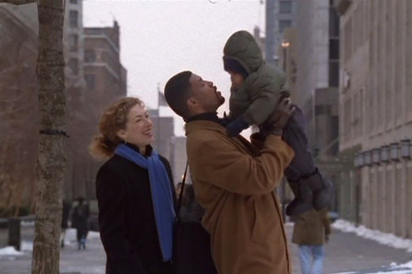 A white woman smiles next to a Black man, who holds up his child.