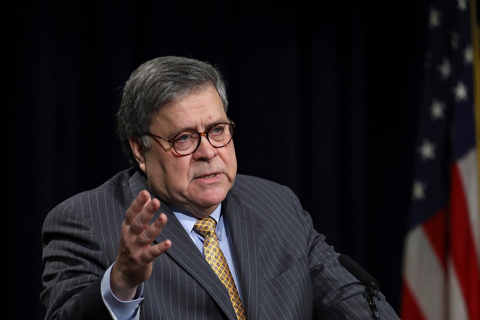 William Barr holds his hand up while standing behind a podium.