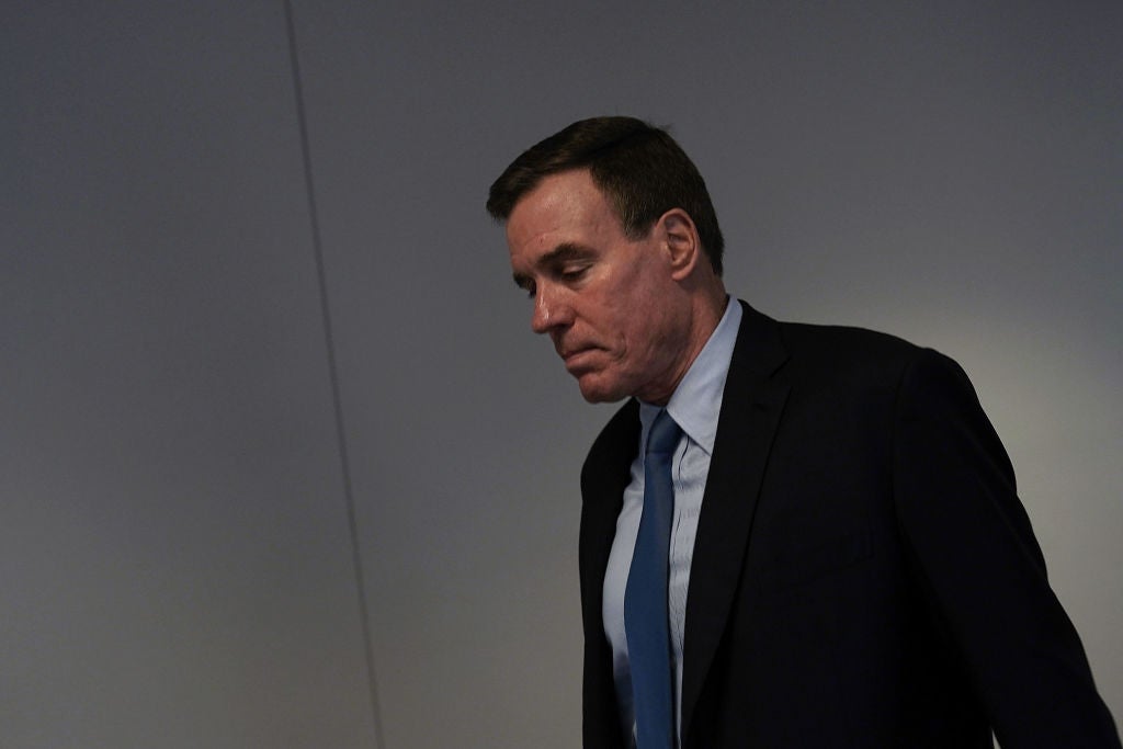 Mark Warner looks downward while walking in what appears to be a dark hallway or stairwell.