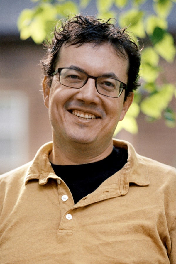 Author Andrew Leland, a white man with black-framed glasses and wearing an orange polo shirt, smiles by a tree.