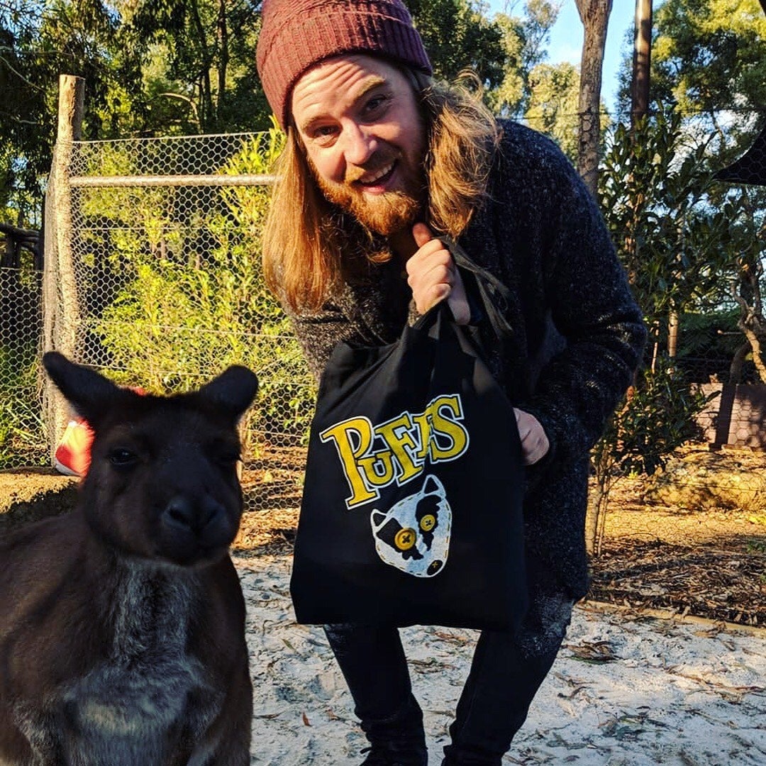 A man with long hair and a beard stands smiling next to a kangaroo.