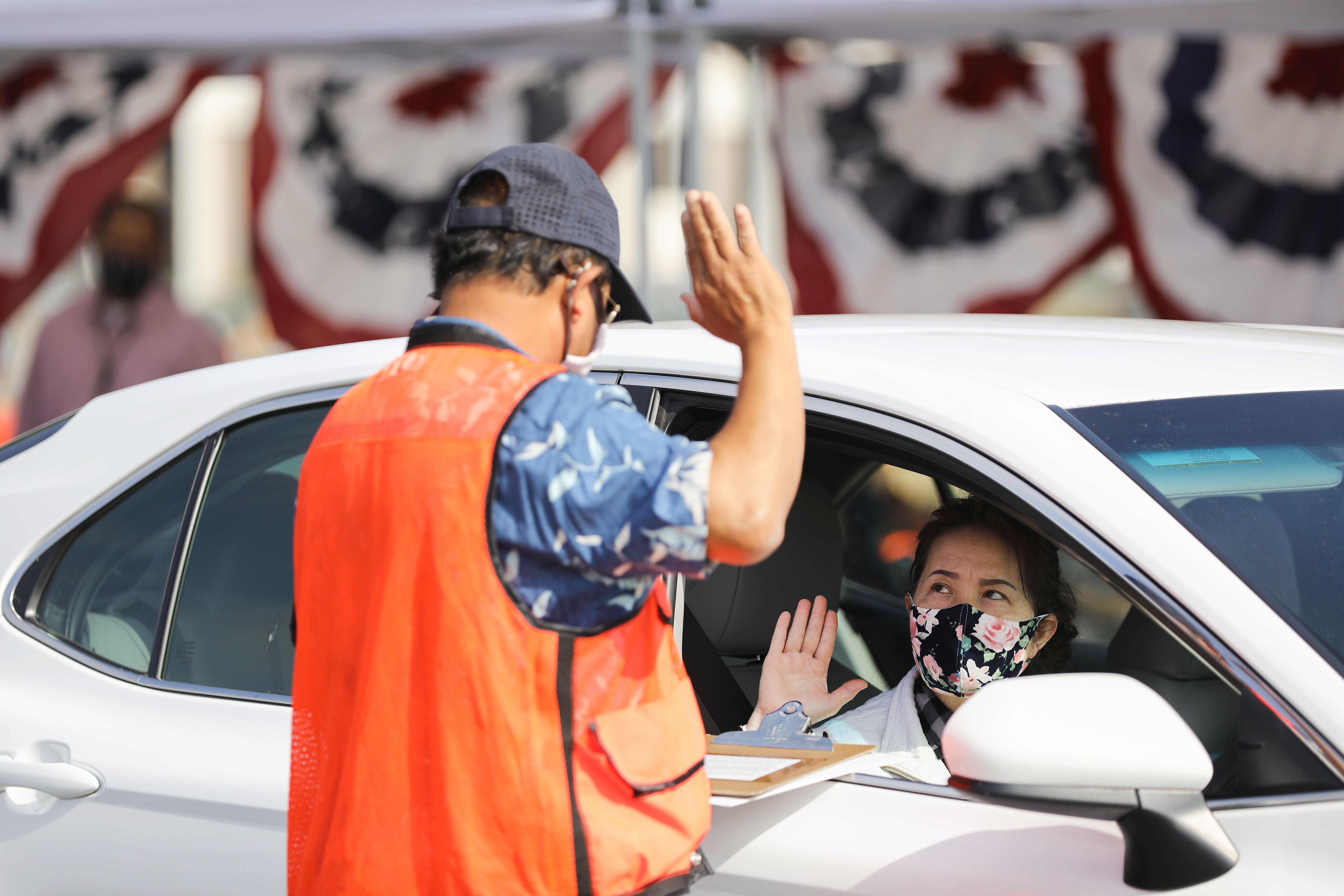 A woman raises her right hand while sitting in a car during drive-in naturalization ceremony in Santa Ana, California. 