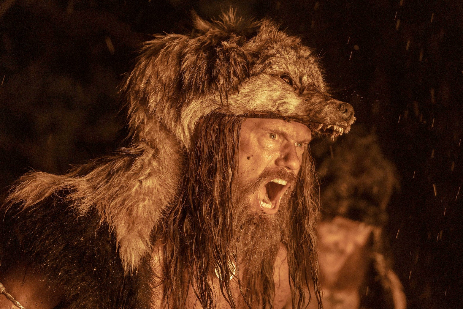 Alexander Skarsgard wears a wolf head and screams in a trance, his face ablaze with the light from a bonfire