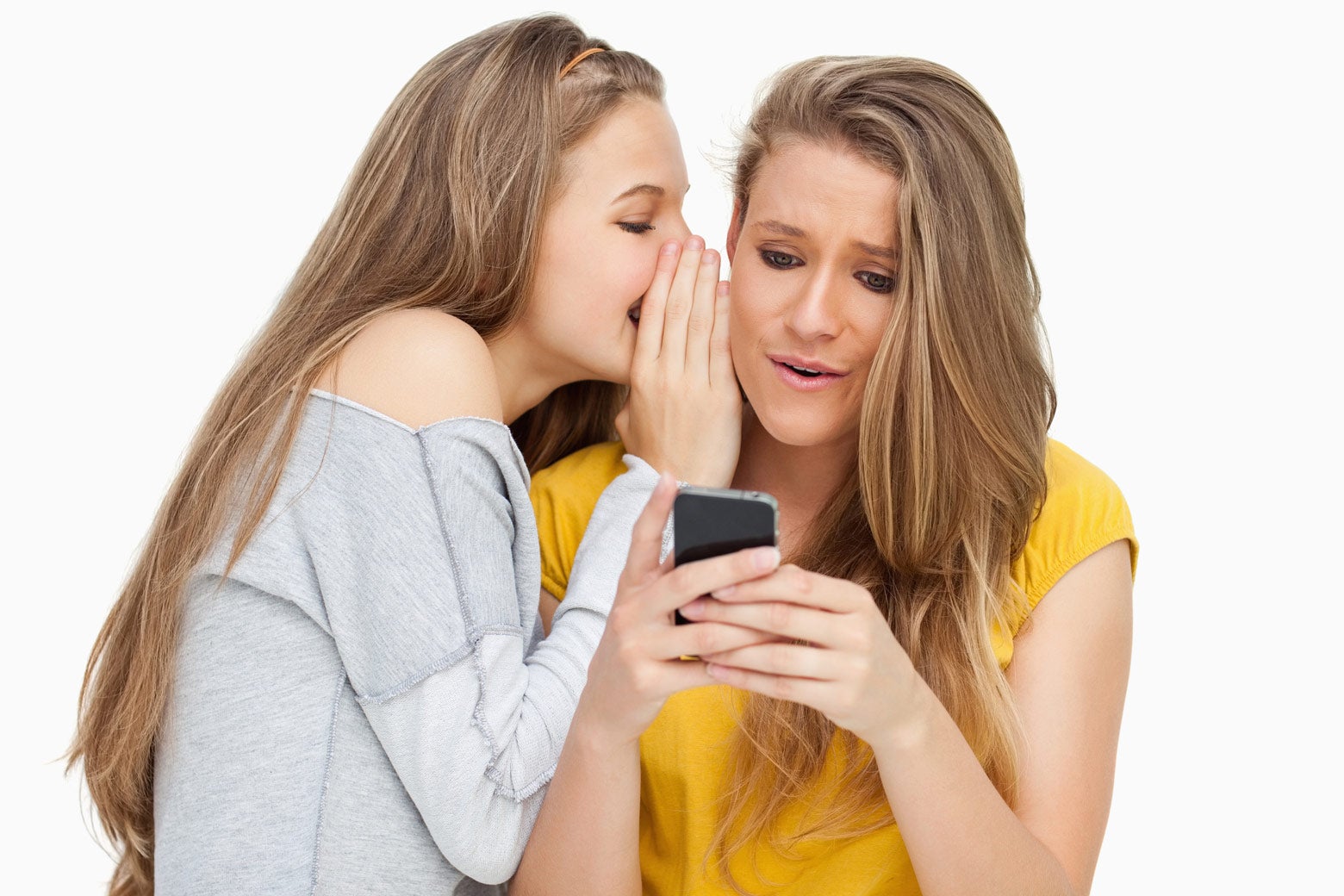 Two young women whispering while looking at a smartphone.
