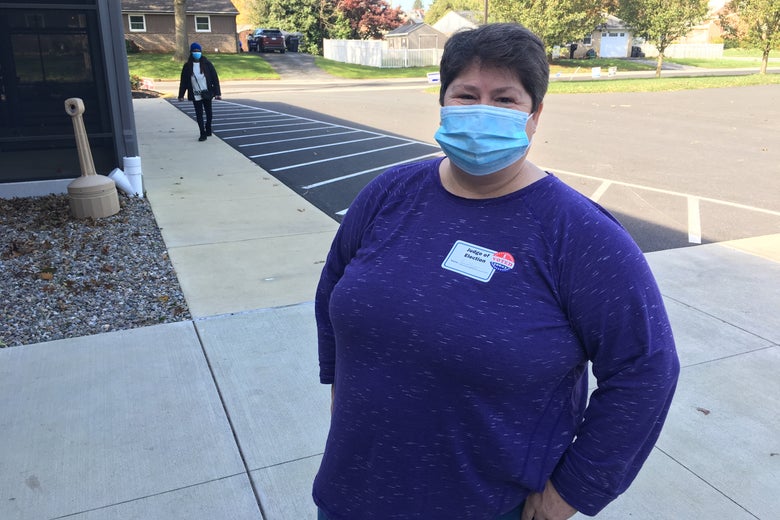 Woman wearing a mask smizes while standing outside on a sidewalk