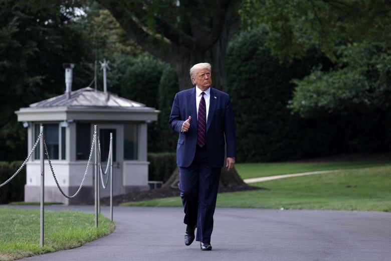 Trump gives a thumbs-up sign while walking on a paved path outside the White House.