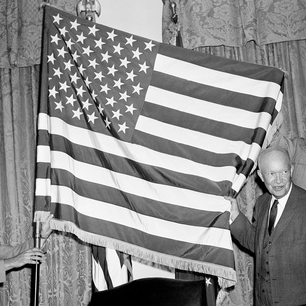 Eisenhower holds onto the edge of the 50-stars flag as it is displayed on a pole inside the White House.