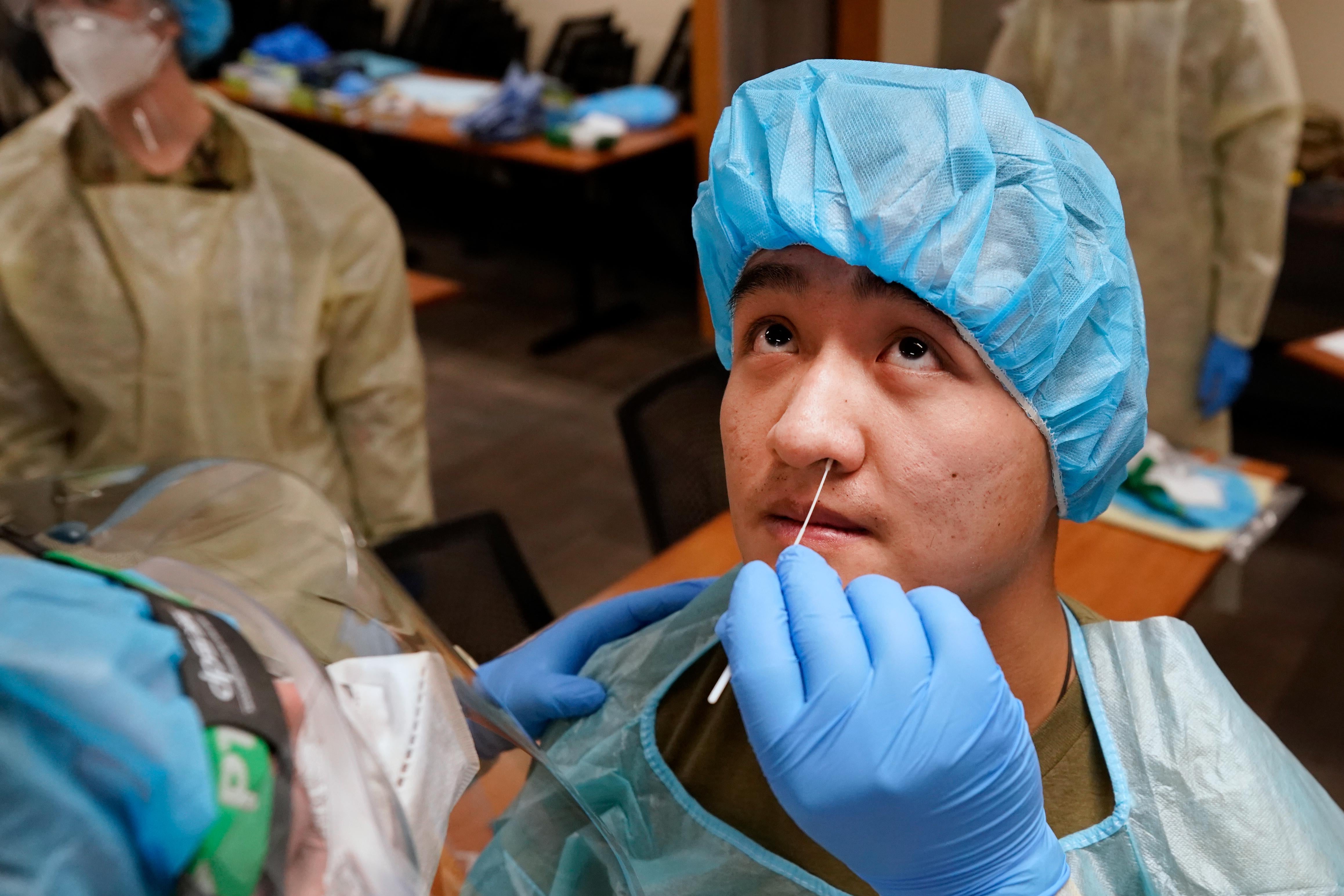 A Utah National Guard member wearing PPE inserts a swab in the nose of another member in PPE to test for COVID-19, with others wearing PPE in the background