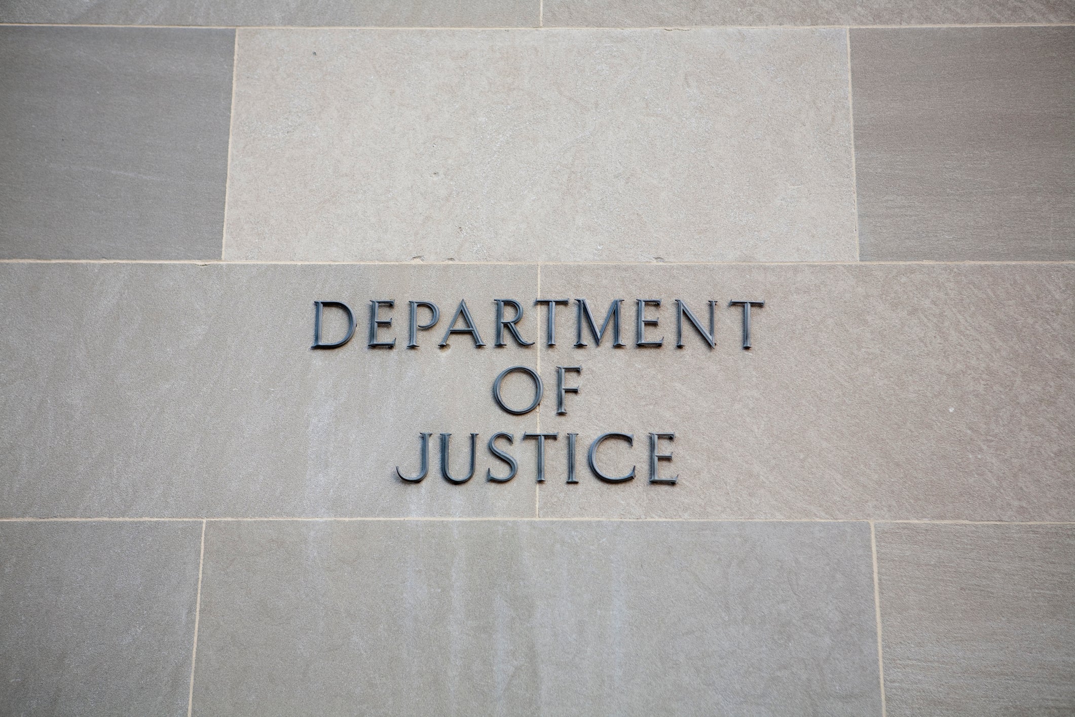 The words "Department of Justice" against a gray slate wall.