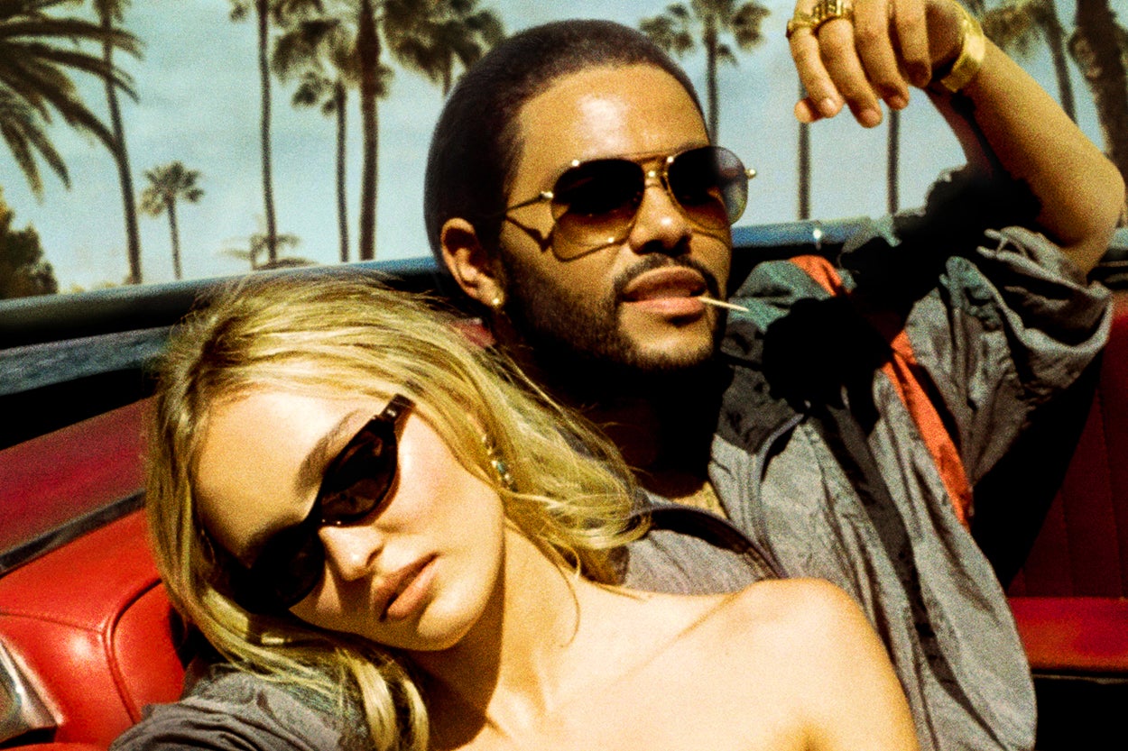 She leans back against him in the red-leather backseat of a vintage-looking car. They both wear sunglasses and gold jewelry, and palm trees can be seen in the backdrop behind them.