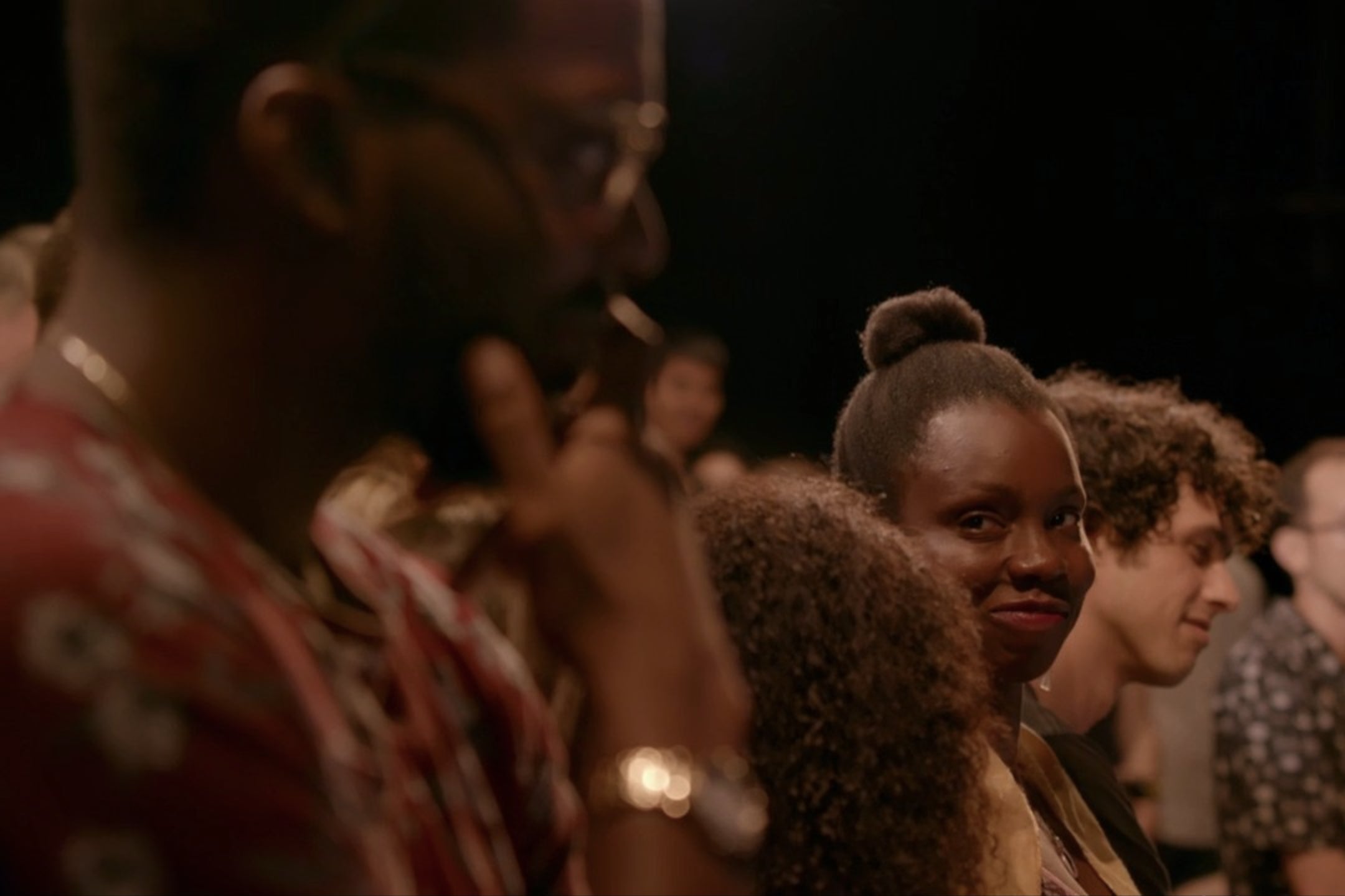 Adepero Oduye, stands in a theater audience, smiling at another person in the foreground.