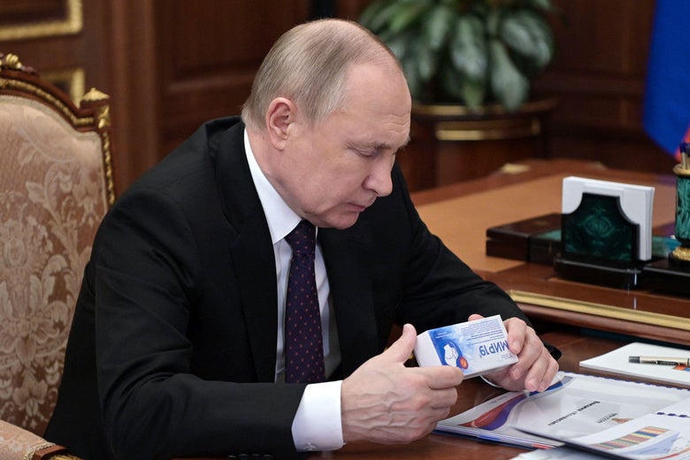 Putin sits at a desk and holds a small box.
