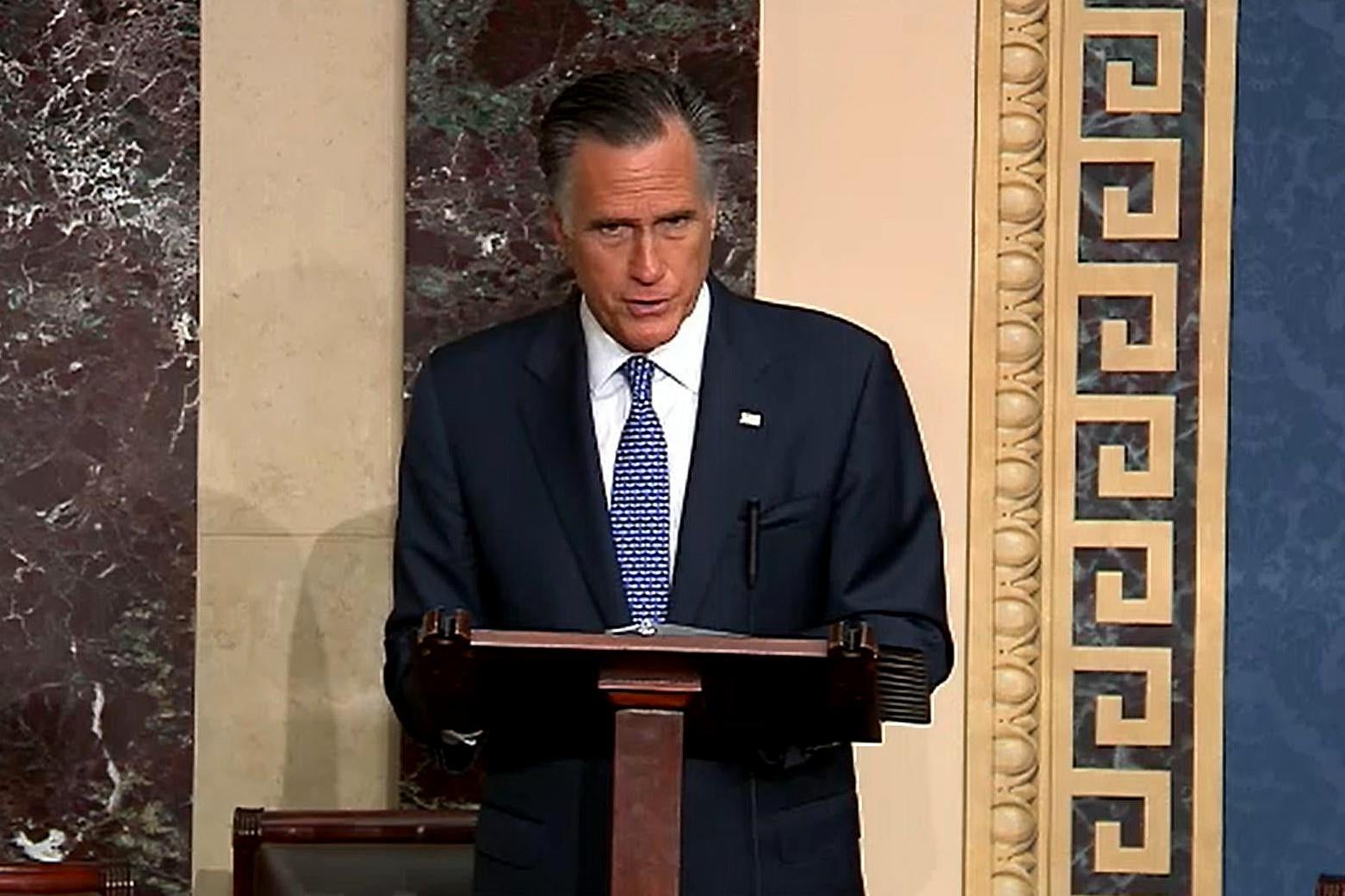 Romney speaks at a podium, looking solemn, in the Senate chamber.