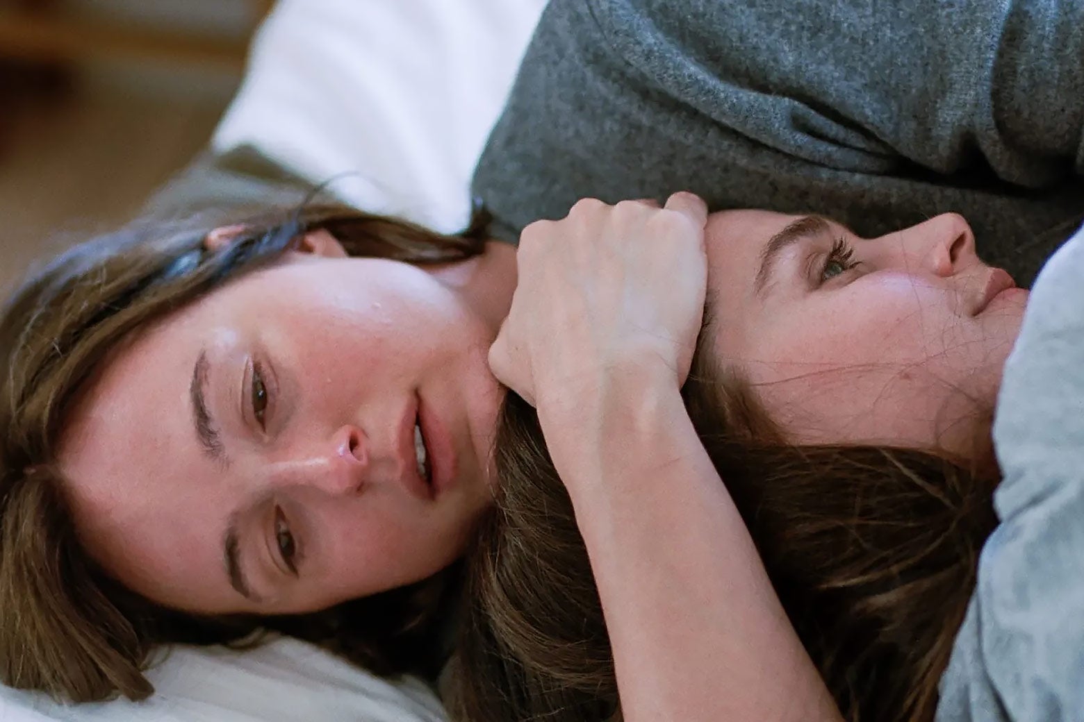 Two upset young women comfort each other while lying in bed. 