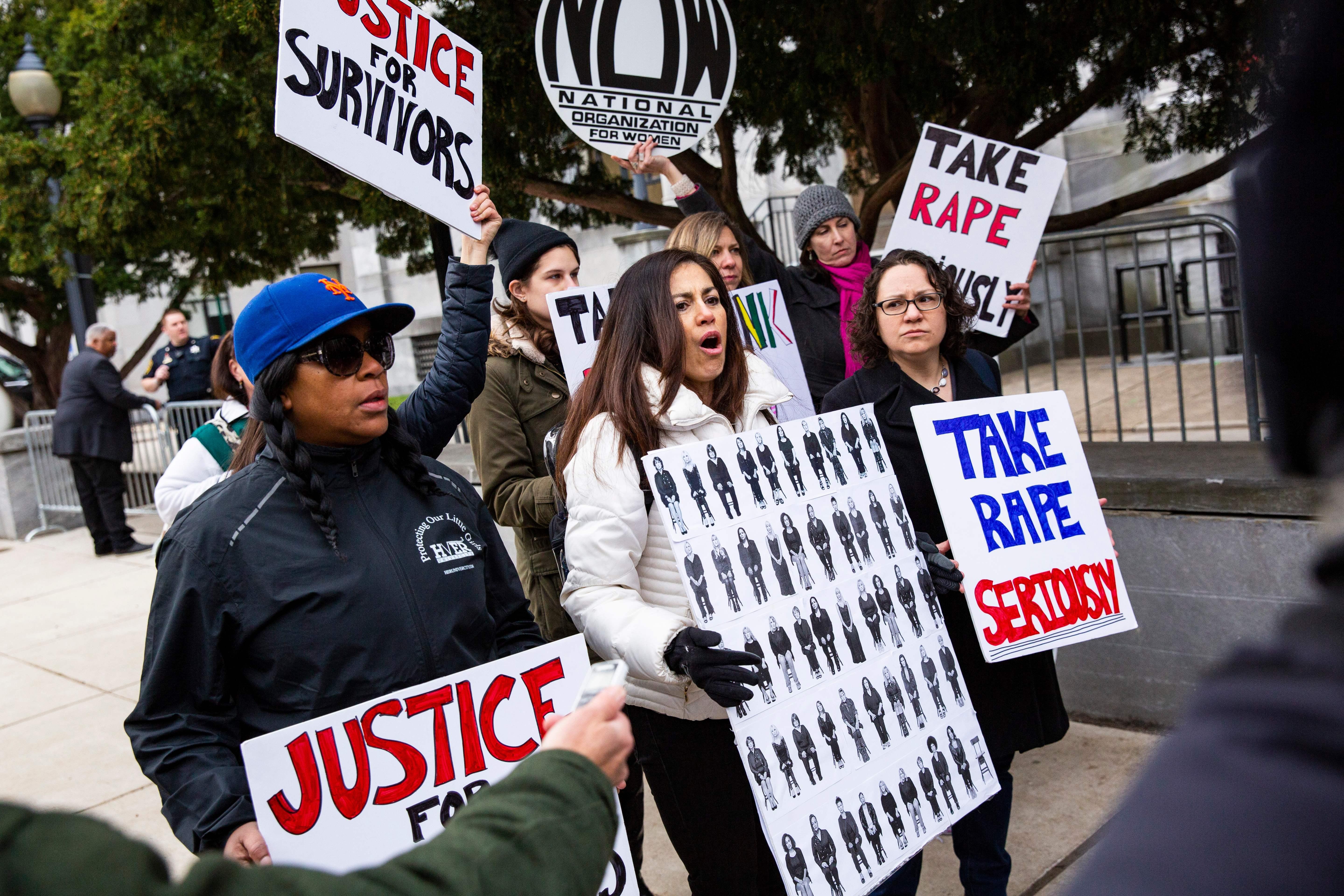 Protesters hold signs saying things like, "Take rape seriously."