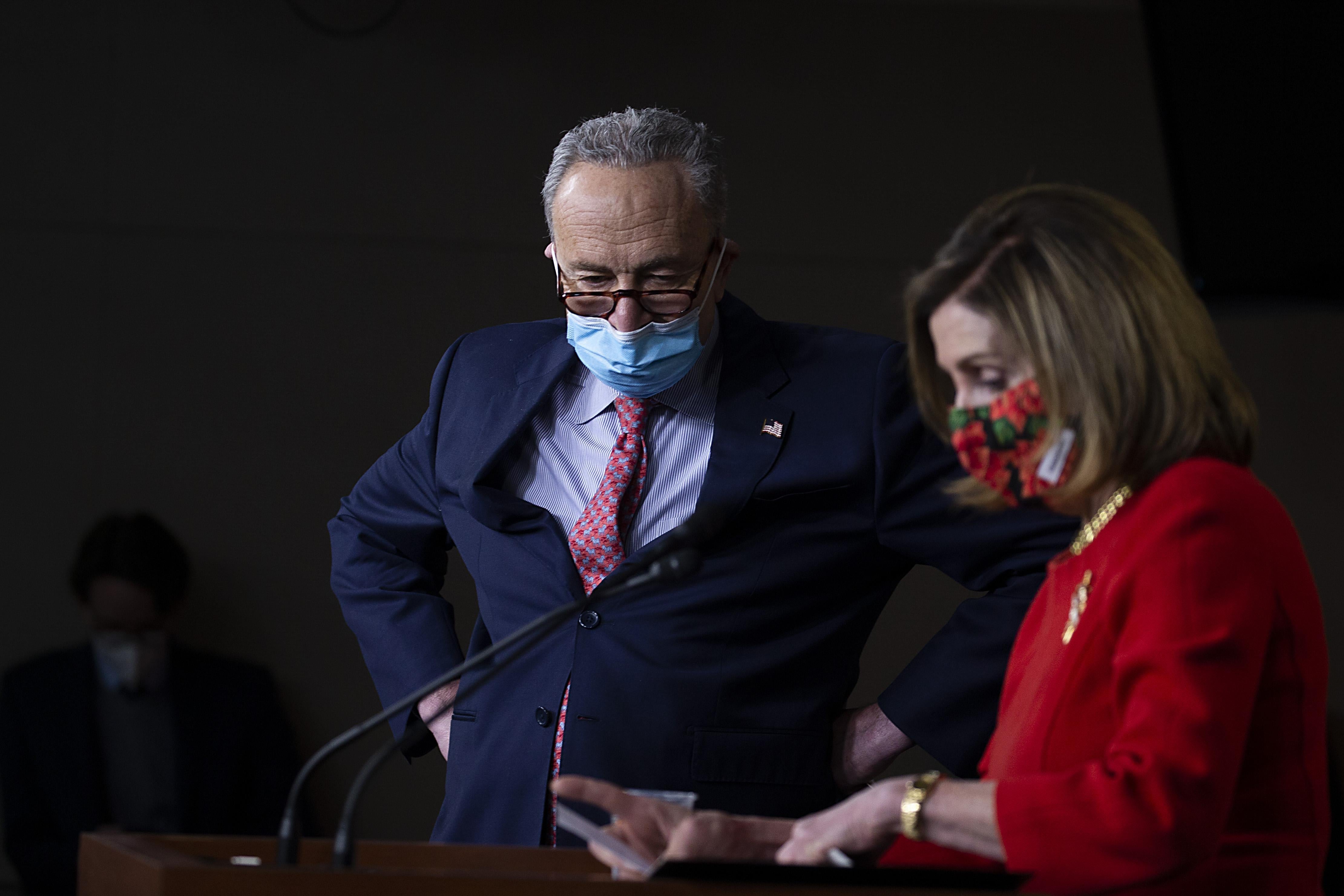 Chuck Schumer and Nancy Pelosi look at a podium while wearing masks.